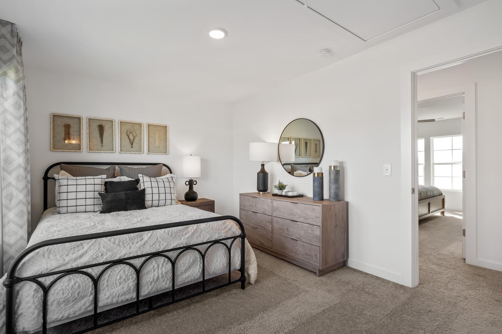 Neutral-toned primary bedroom at The Towns at Red River in Gallatin TN with black metal bed, dresser, and round mirror
