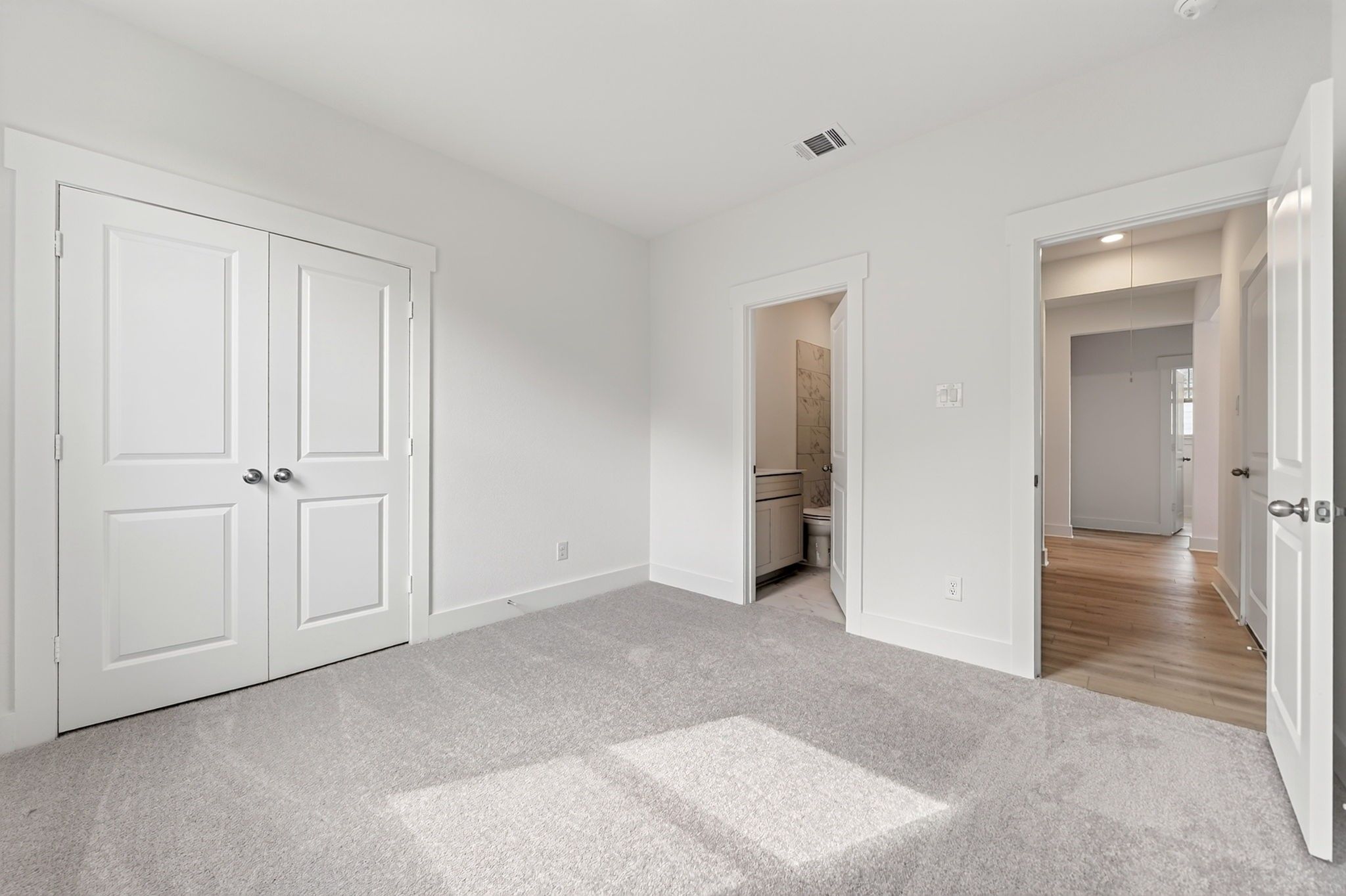 Bright bedroom with gray carpet, double-door closet, and en-suite bath in Davidson Homes Holly F plan, Josephine, Texas