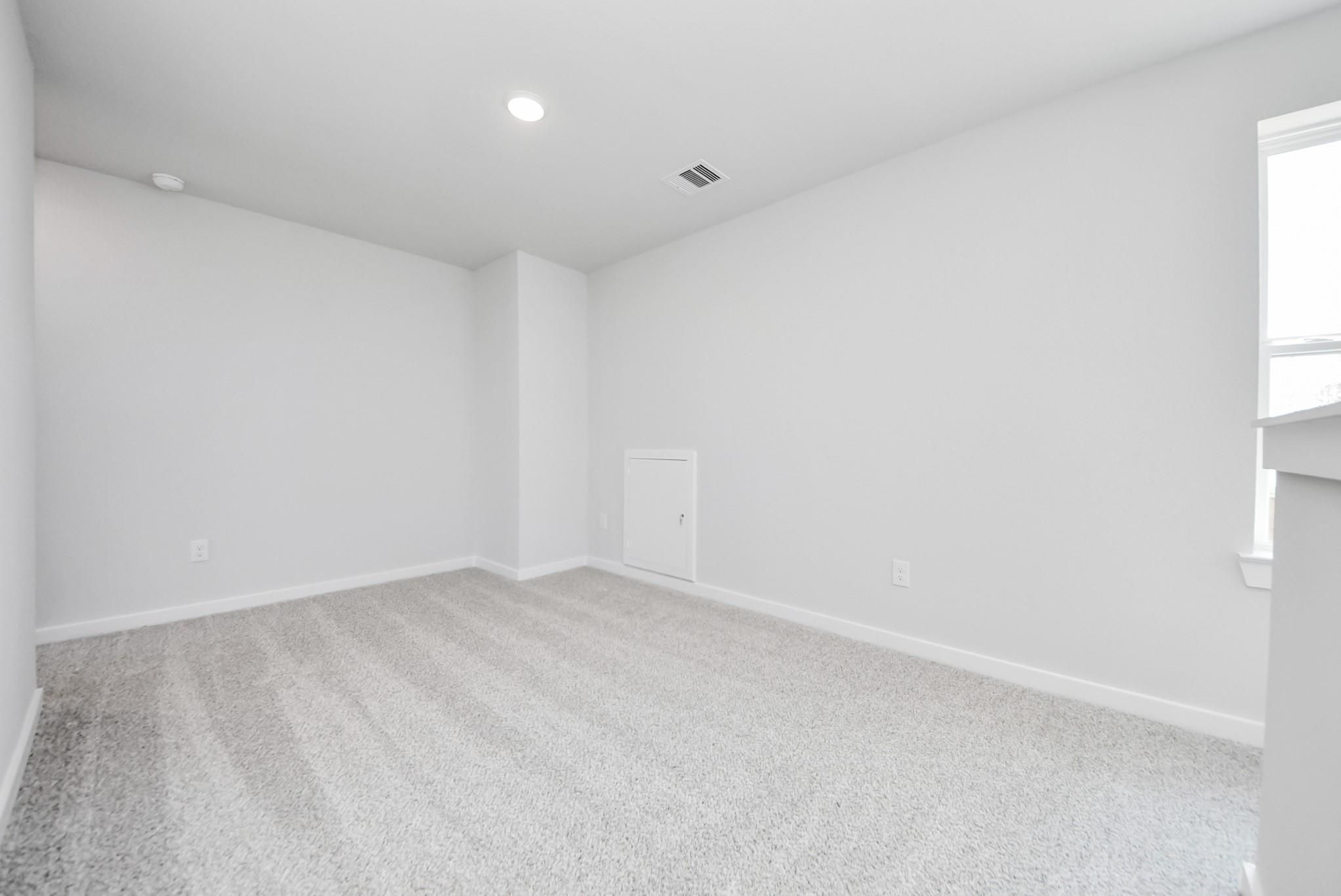 Bright, carpeted bedroom with neutral walls and attic access in The Blanco F floor plan at Spring Branch Crossing, Conroe.