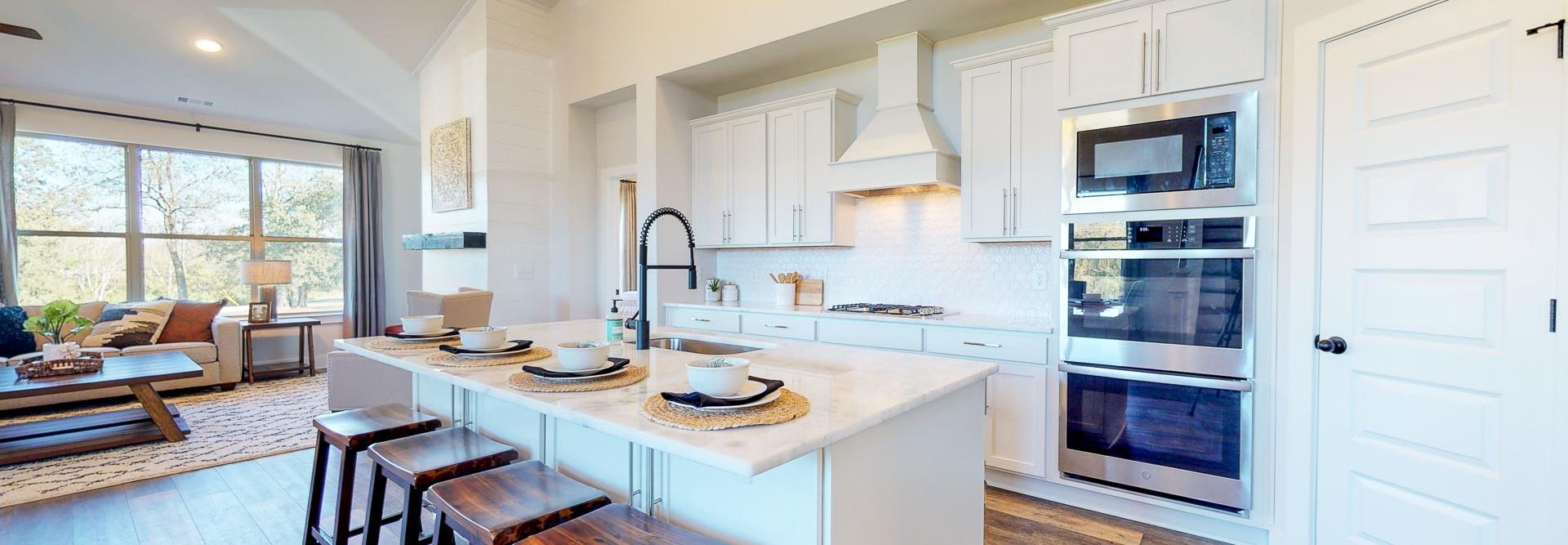 Open-concept kitchen at Liberty Creek in Gallatin TN featuring white island, wood bar stools, stainless appliances, and hardwood floors