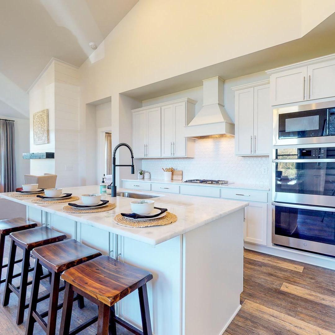 Open-concept kitchen at Liberty Creek in Gallatin TN featuring white island, wood bar stools, stainless appliances, and hardwood floors