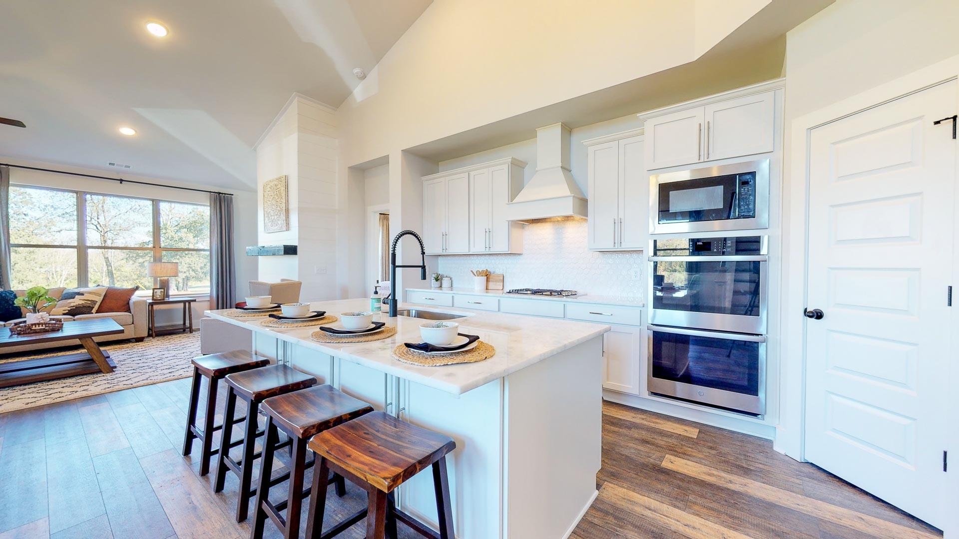 Open-concept kitchen at Liberty Creek in Gallatin TN featuring white island, wood bar stools, stainless appliances, and hardwood floors