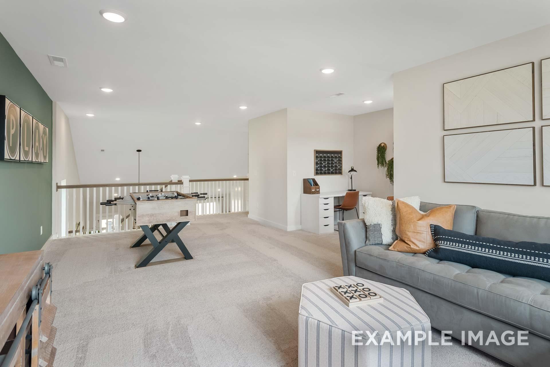 Spacious upstairs loft with gray sofa, striped ottoman, desk, and game table in Davidson Homes The Ridgeport, Gallatin, TN