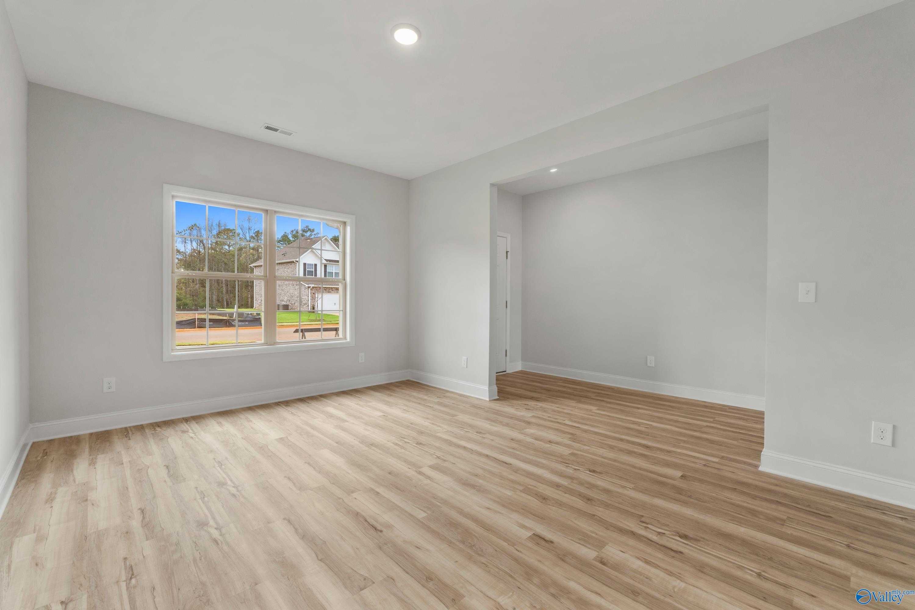 Bright secondary bedroom with light gray walls, hardwood floors, and large window view in Davidson Homes The Chelsea C, Harvest, Alabama