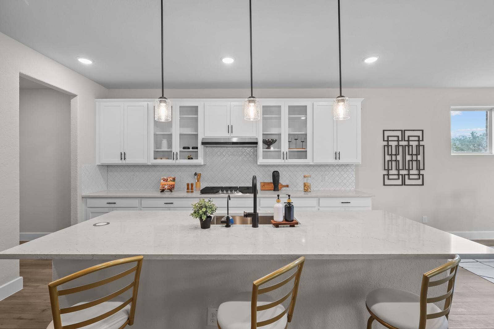 Modern white kitchen in The Belmont with expansive quartz island, sleek cabinetry, and stylish pendant lighting.