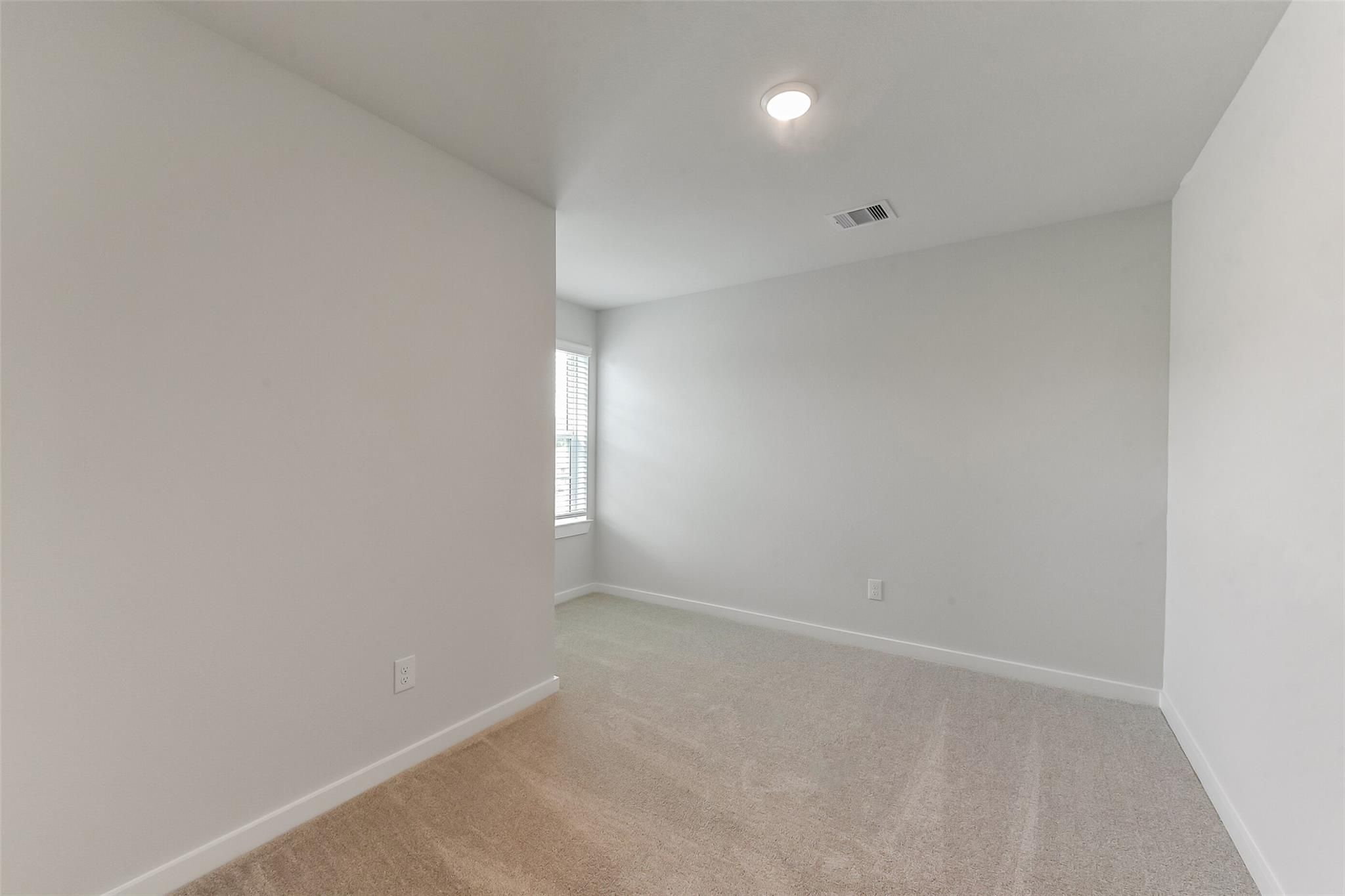 Spacious empty bedroom with neutral gray walls, beige carpet, window blinds, and recessed lighting in Davidson Homes The Sabine F, Dayton, Texas