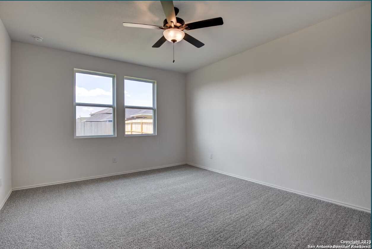 Bright secondary bedroom featuring large windows, ceiling fan, and neutral carpet in Davidson Homes The Daphne H, Seguin, Texas