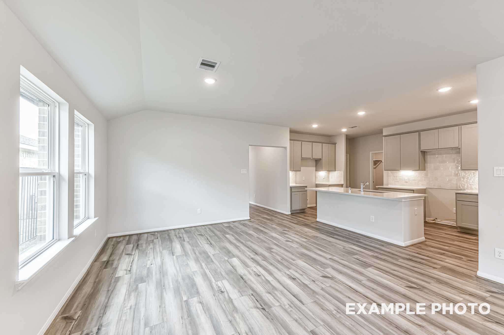 Open-concept kitchen in The Laguna A with white shaker cabinets, quartz counters, large island, and luxury vinyl plank flooring