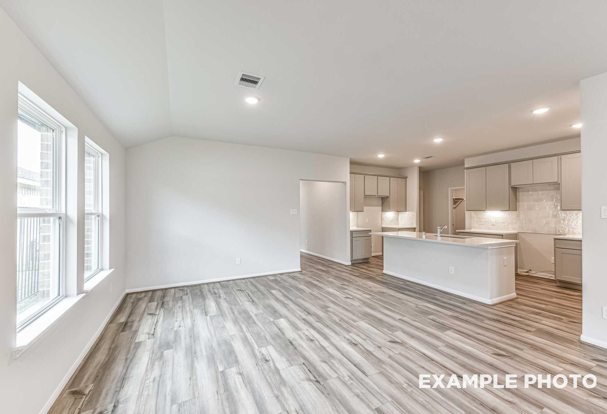 Open-concept kitchen in The Laguna A with white shaker cabinets, quartz counters, large island, and luxury vinyl plank flooring