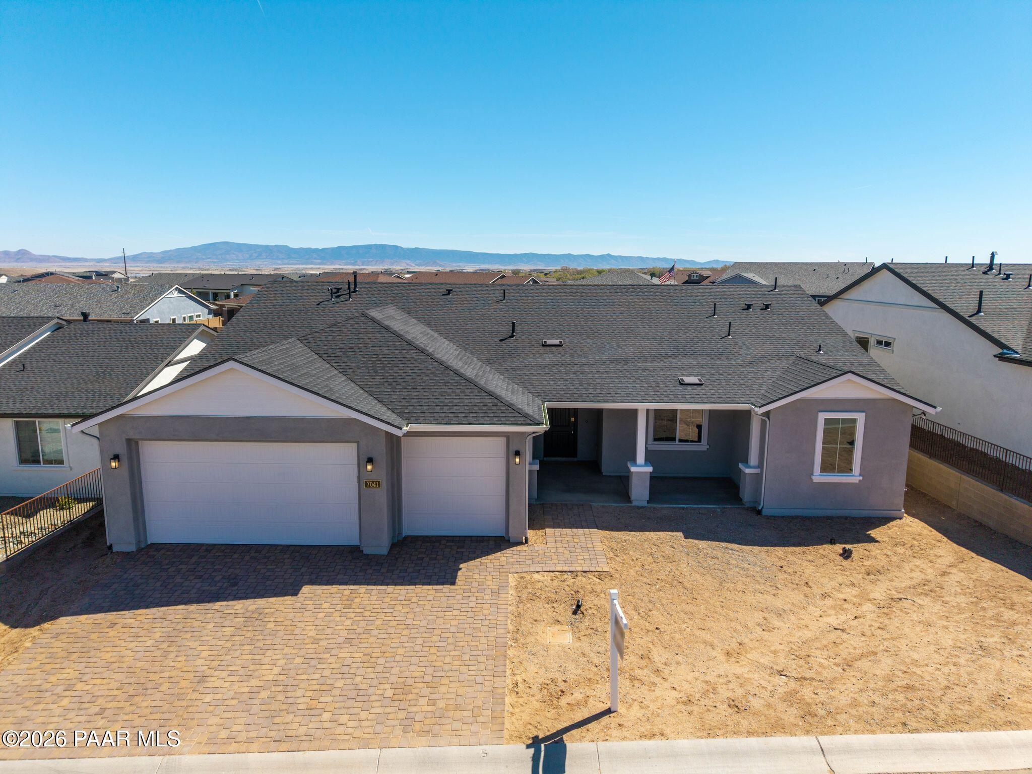 Aerial view of modern single-story 3-car garage home with gray exterior, paver driveway, and mountain backdrop in Westwood, Prescott, Arizona - Davidson Homes The Monarch A