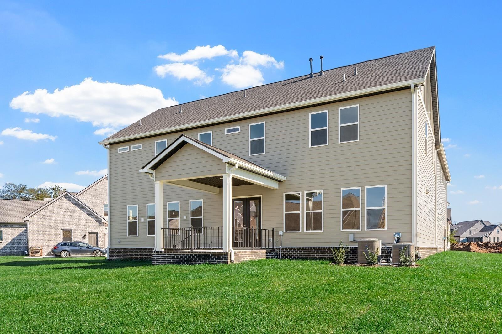 Two-story beige home with covered front porch, large windows, and green lawn in Davidson Homes The Alston A, Shelton Square, Murfreesboro, TN