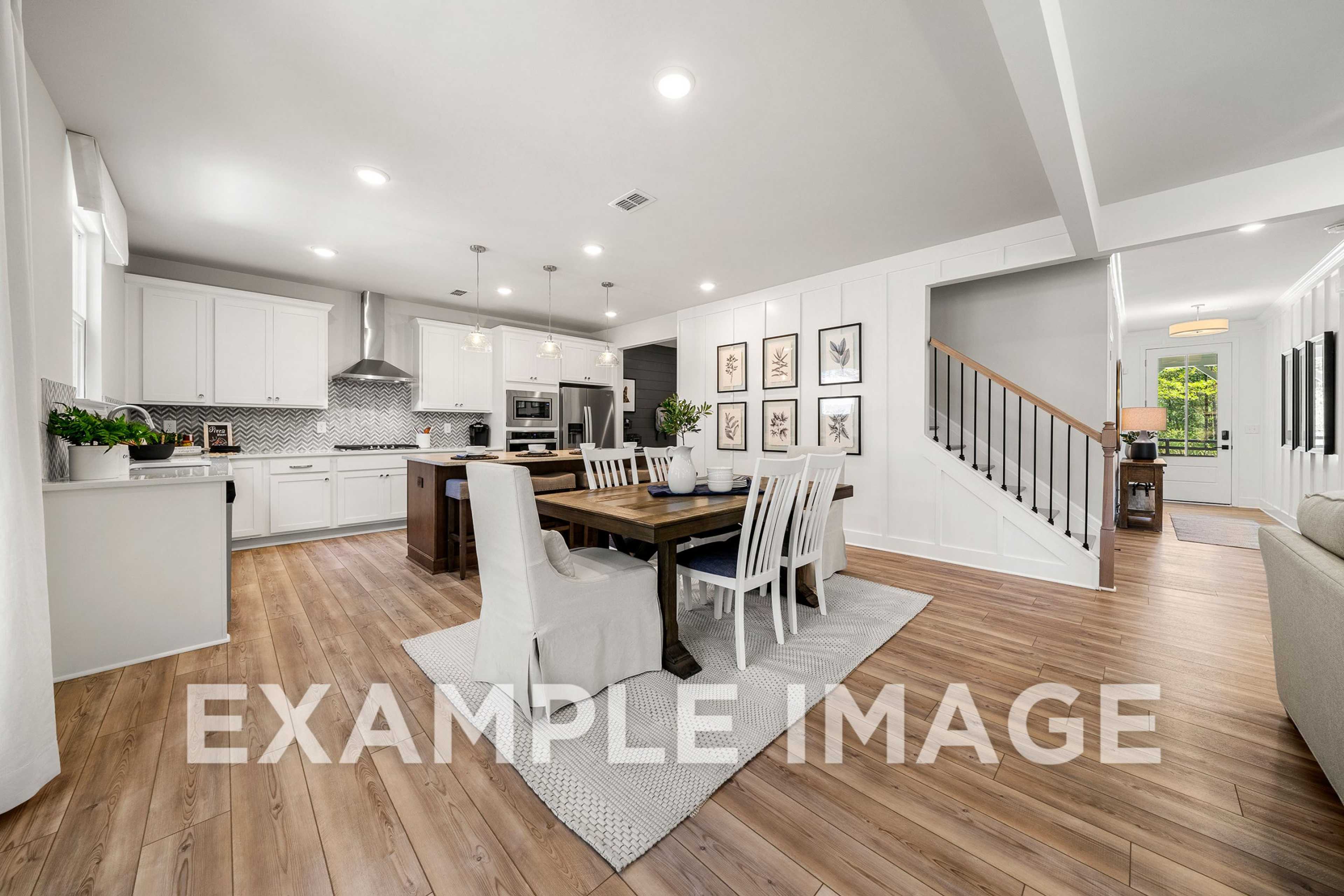 Spacious open-concept kitchen and dining in The Hickory A featuring white cabinetry, large island, farmhouse table, staircase, and living area
