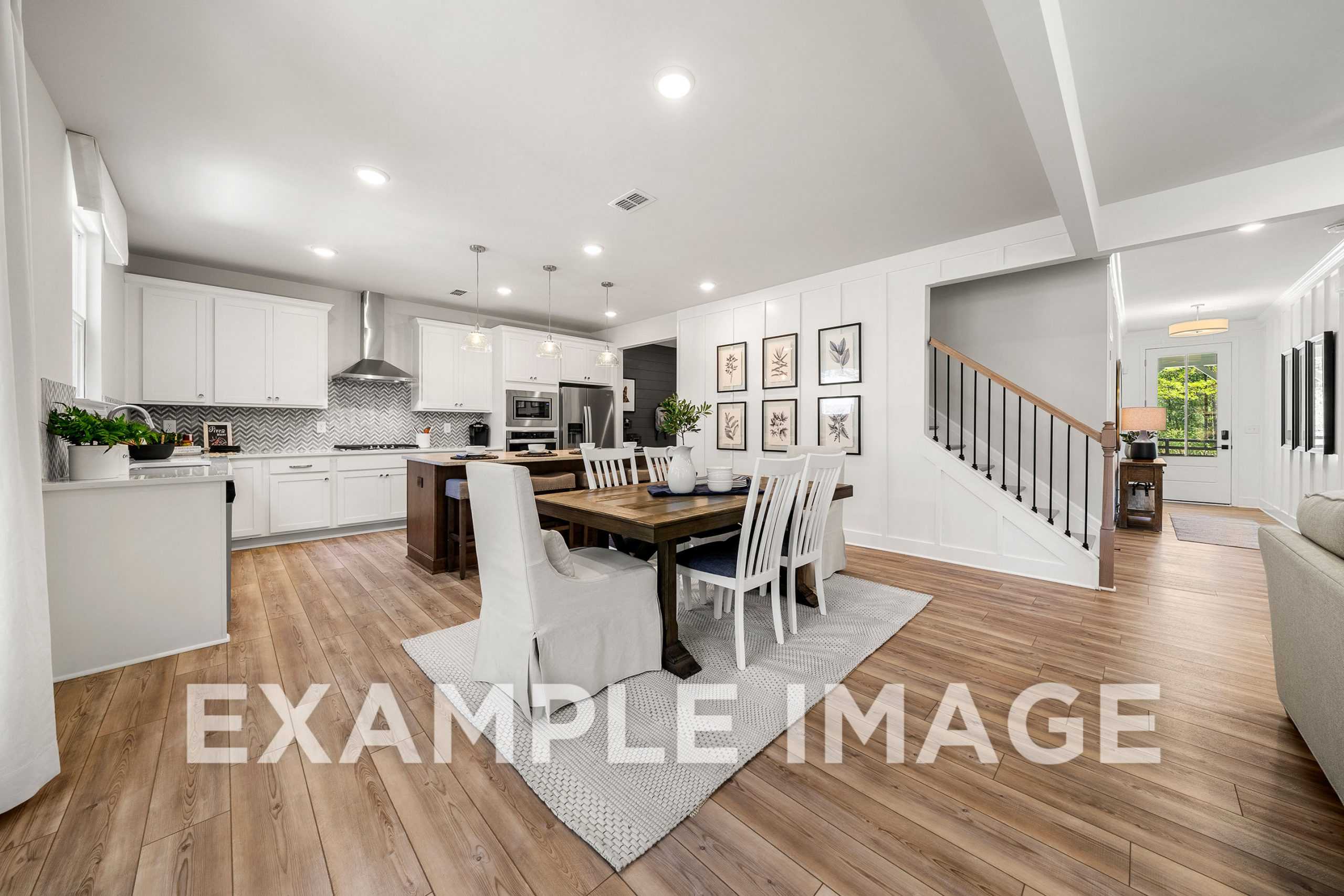 Spacious open-concept kitchen and dining in The Hickory A featuring white cabinetry, large island, farmhouse table, staircase, and living area