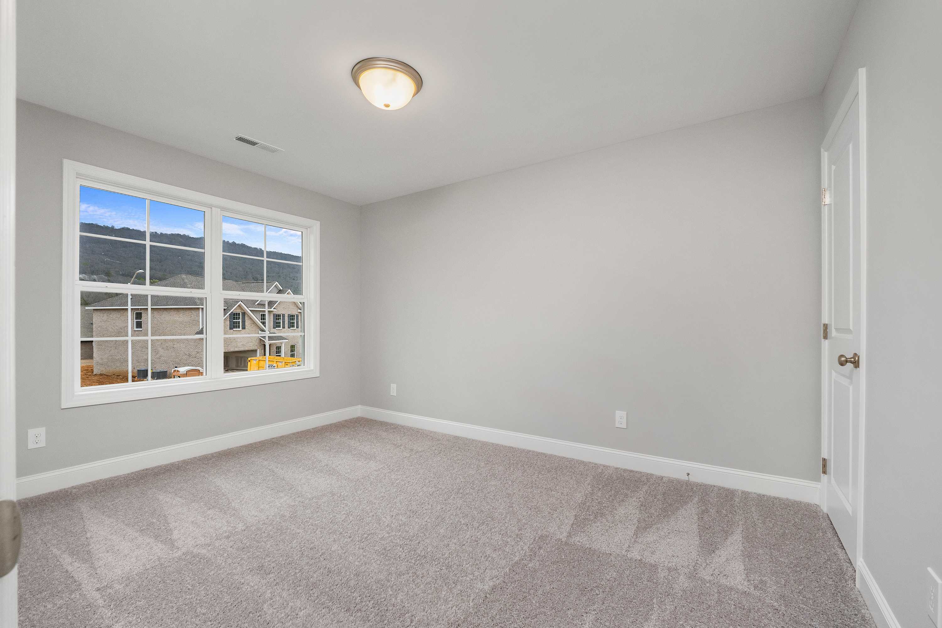 Spacious upstairs bedroom in The Aiken home featuring gray walls, beige carpet, large window with neighborhood view