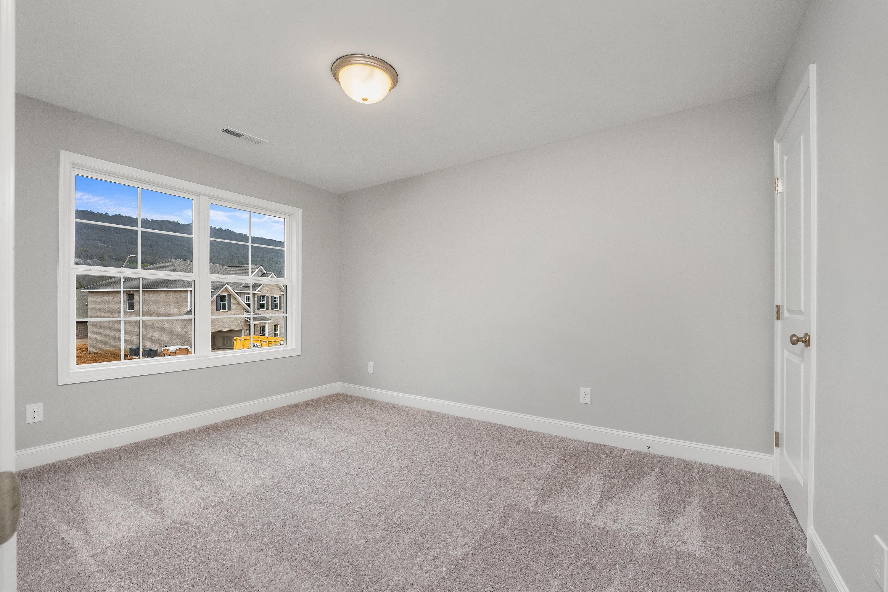 Spacious upstairs bedroom in The Aiken home featuring gray walls, beige carpet, large window with neighborhood view