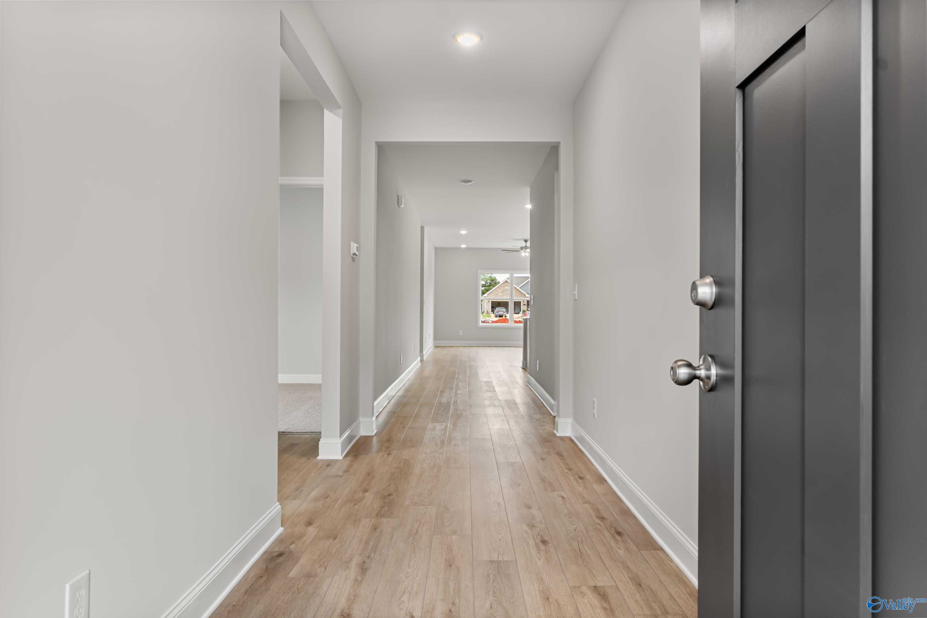 Bright hallway with light oak floors, white walls, black door, and window in The Daphne C 4-bedroom home, Athens Alabama