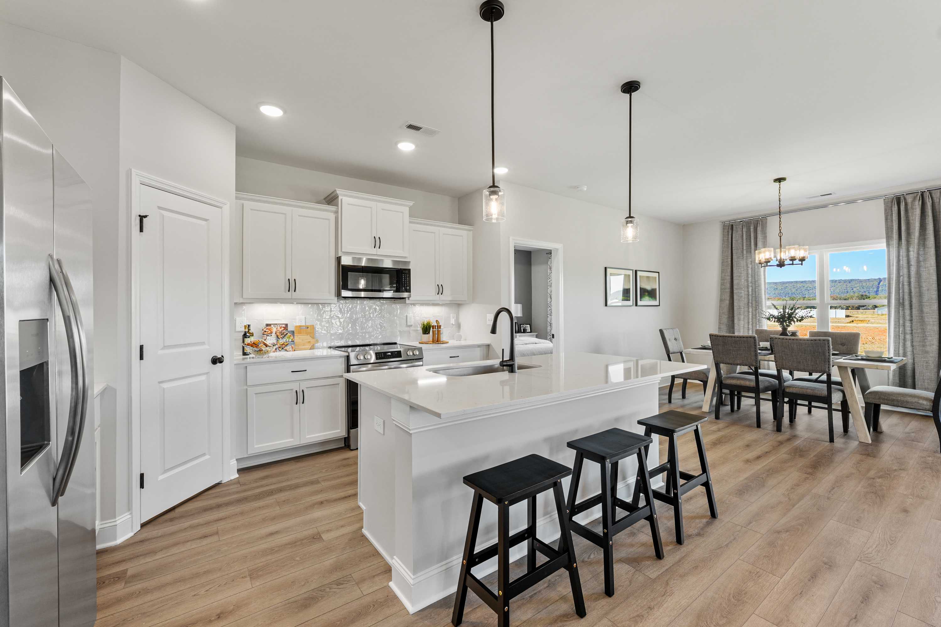 Spacious open-concept kitchen in Ramsay Cove, Owens Cross Roads AL with white cabinets, quartz island, black stools, hardwood floors, and dining nook
