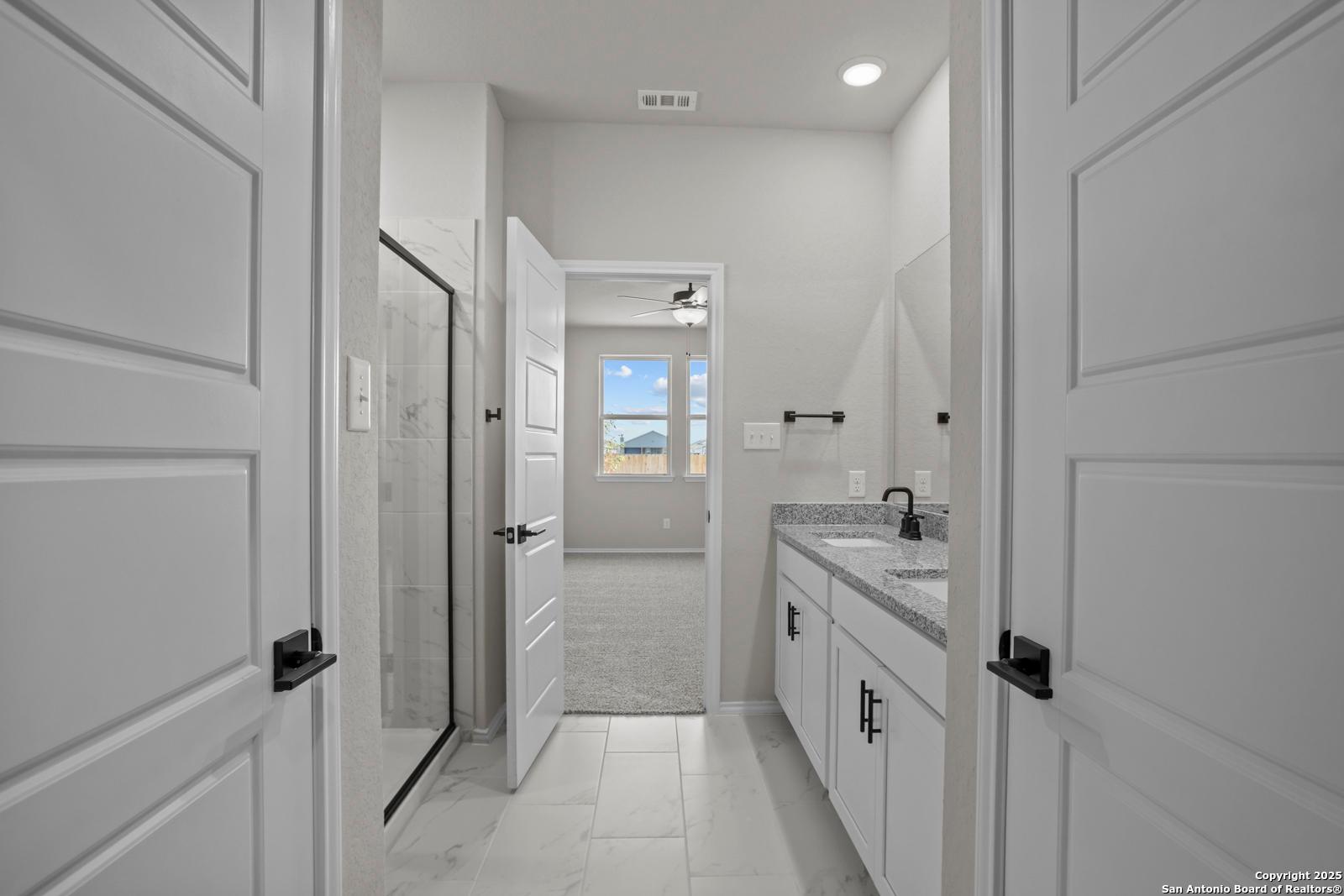 Modern master bathroom featuring walk-in shower, white double vanity, and window view in Davidson Homes The Daphne H, Seguin, Texas
