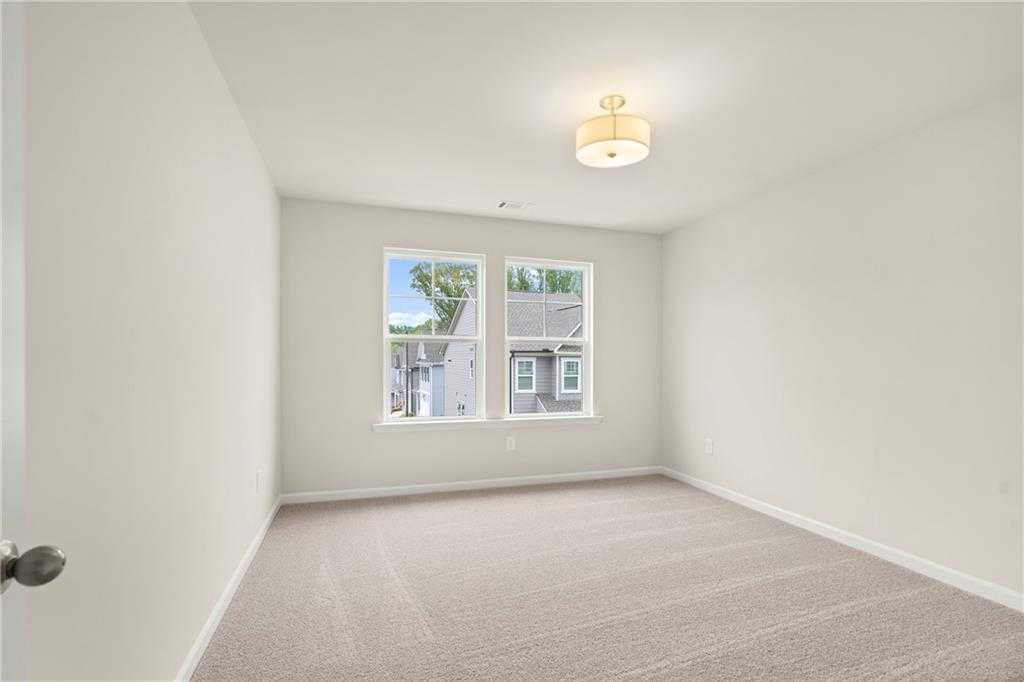 Bright empty secondary bedroom with large windows, neutral walls, and carpet in Davidson Homes The Cary A, Kennesaw, Georgia