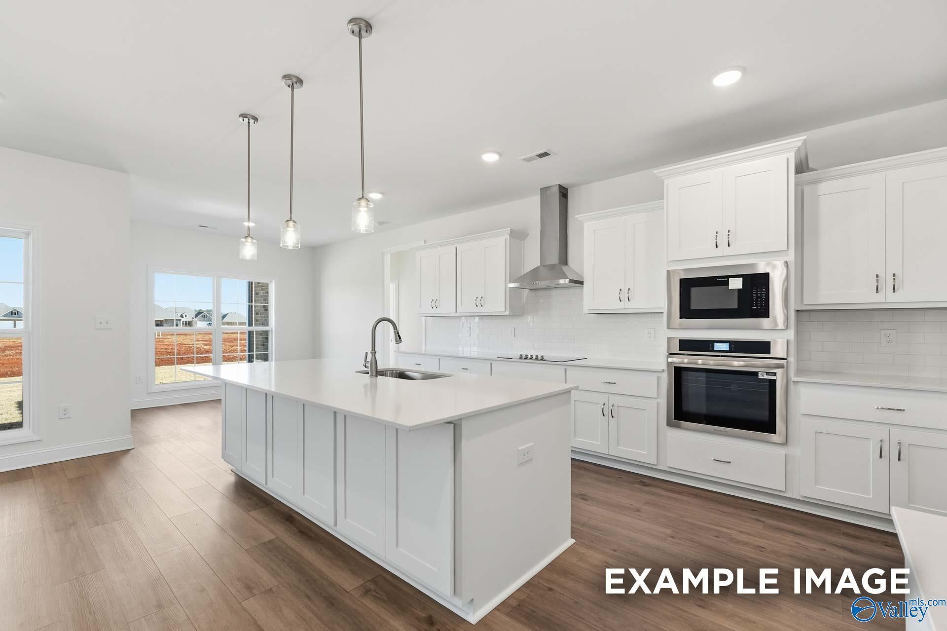 Modern white kitchen with large island and stainless appliances in The Valencia floor plan, Briercreek, Meridianville.