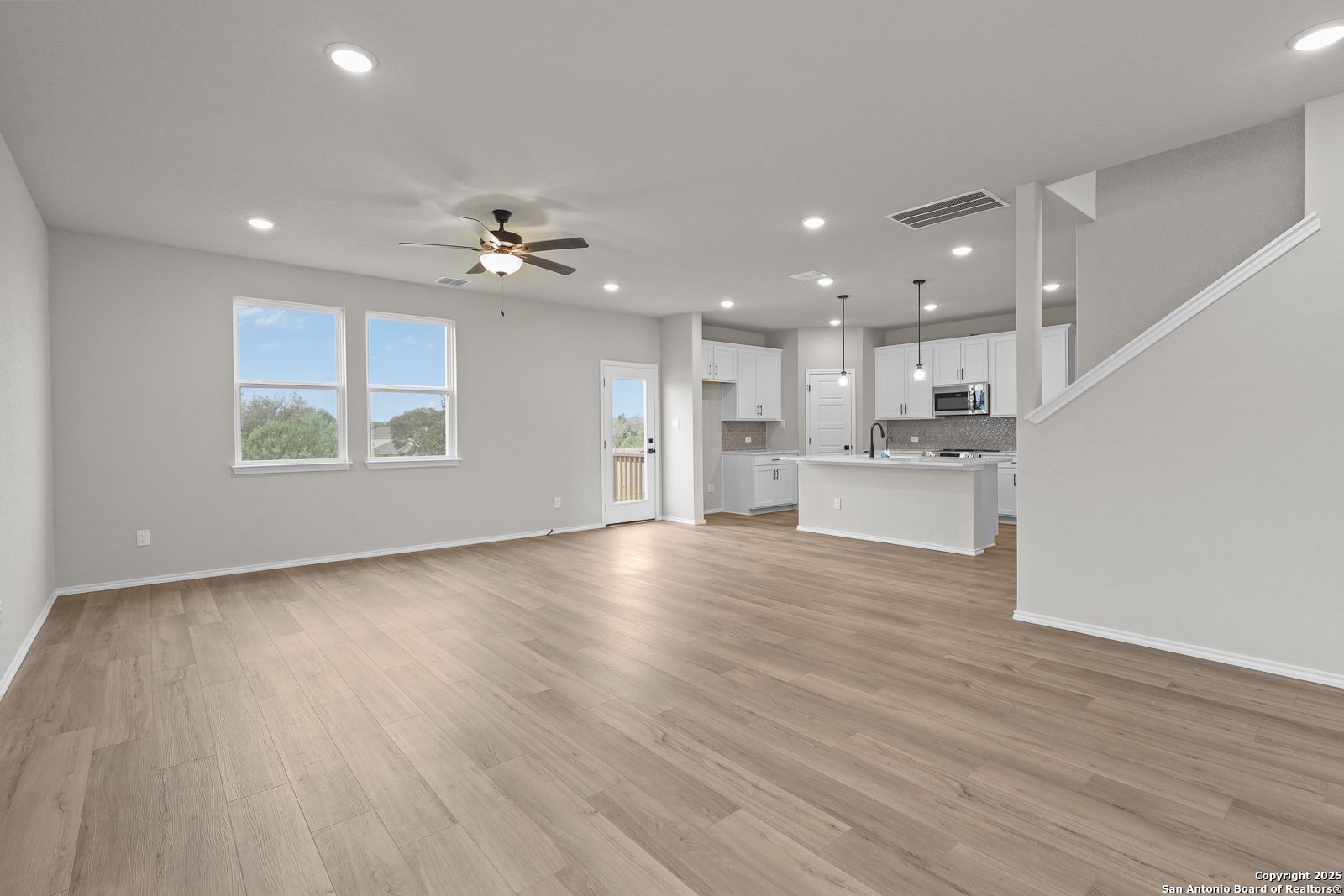 Open-concept living-kitchen with white cabinets, island, stainless microwave, hardwood floors, ceiling fan in Davidson Homes The Murray J, San Antonio