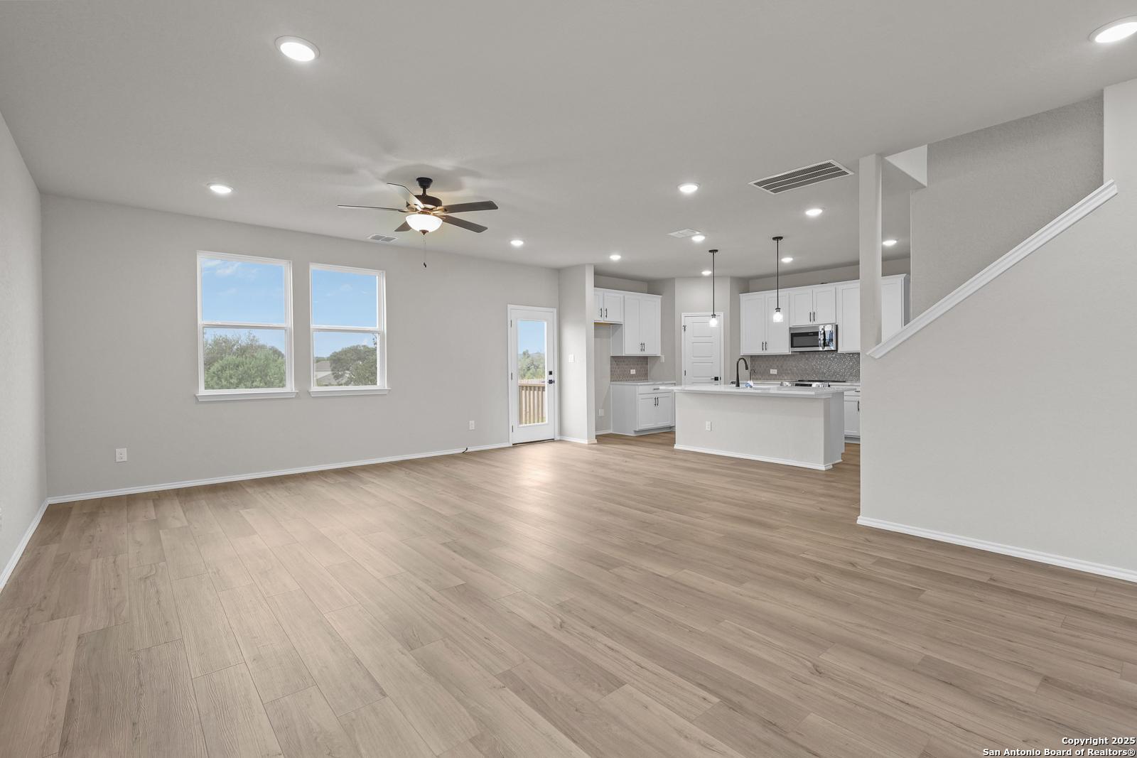 Open-concept living-kitchen with white cabinets, island, stainless microwave, hardwood floors, ceiling fan in Davidson Homes The Murray J, San Antonio