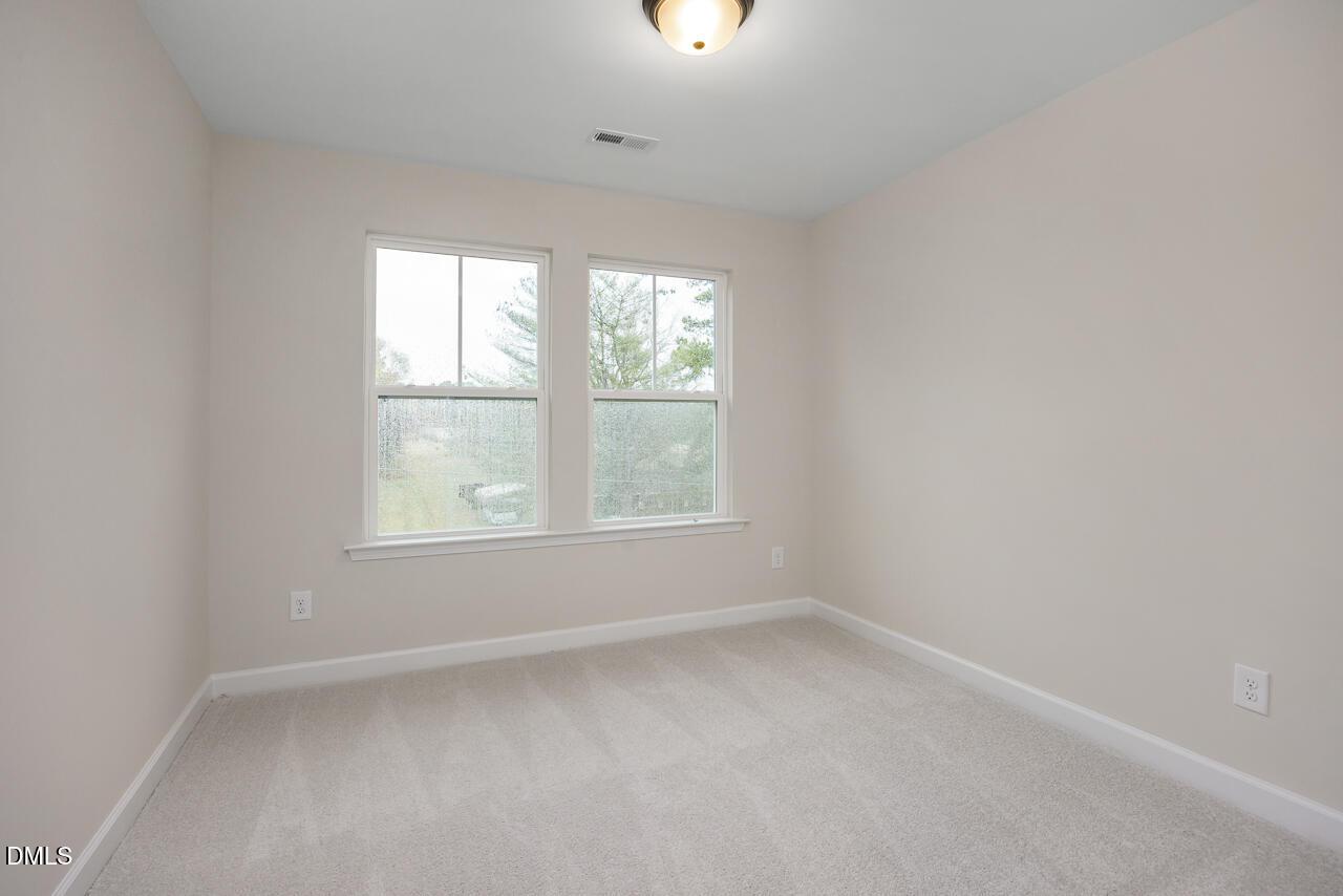 Bright secondary bedroom with beige walls, large double windows, and neutral carpet in Davidson Homes The Mitchell, Knightdale, NC