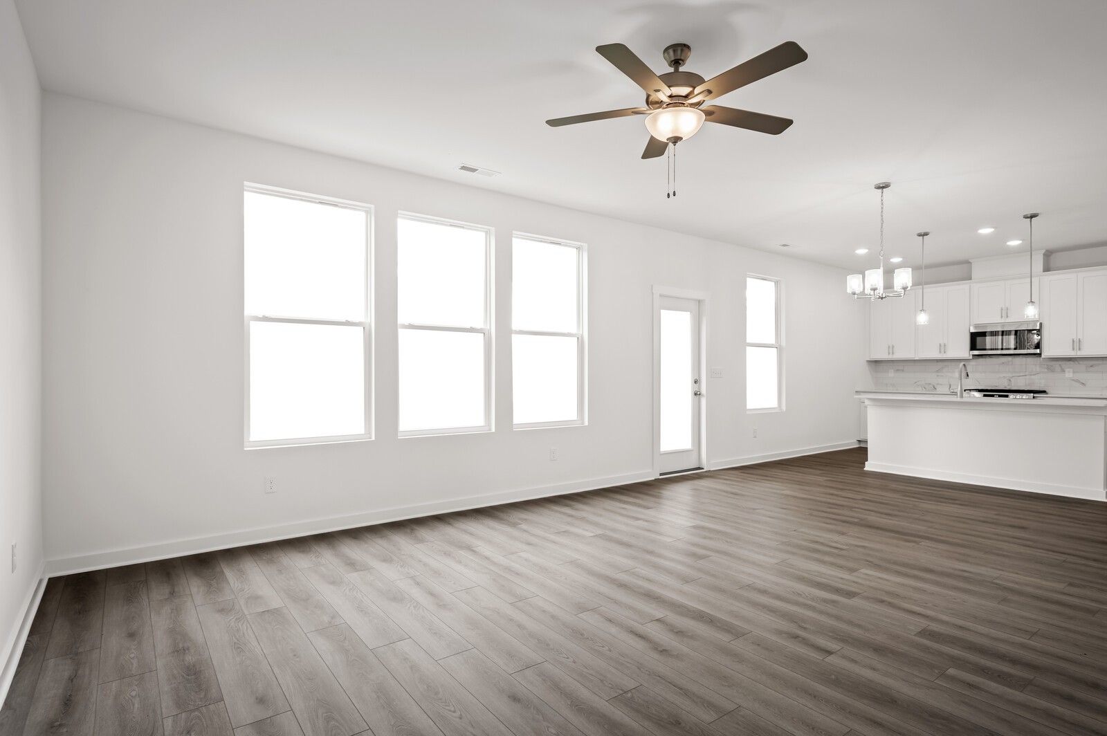 Bright open-concept living area with wood-look flooring and modern kitchen in The Logan C home at Calista Farms.