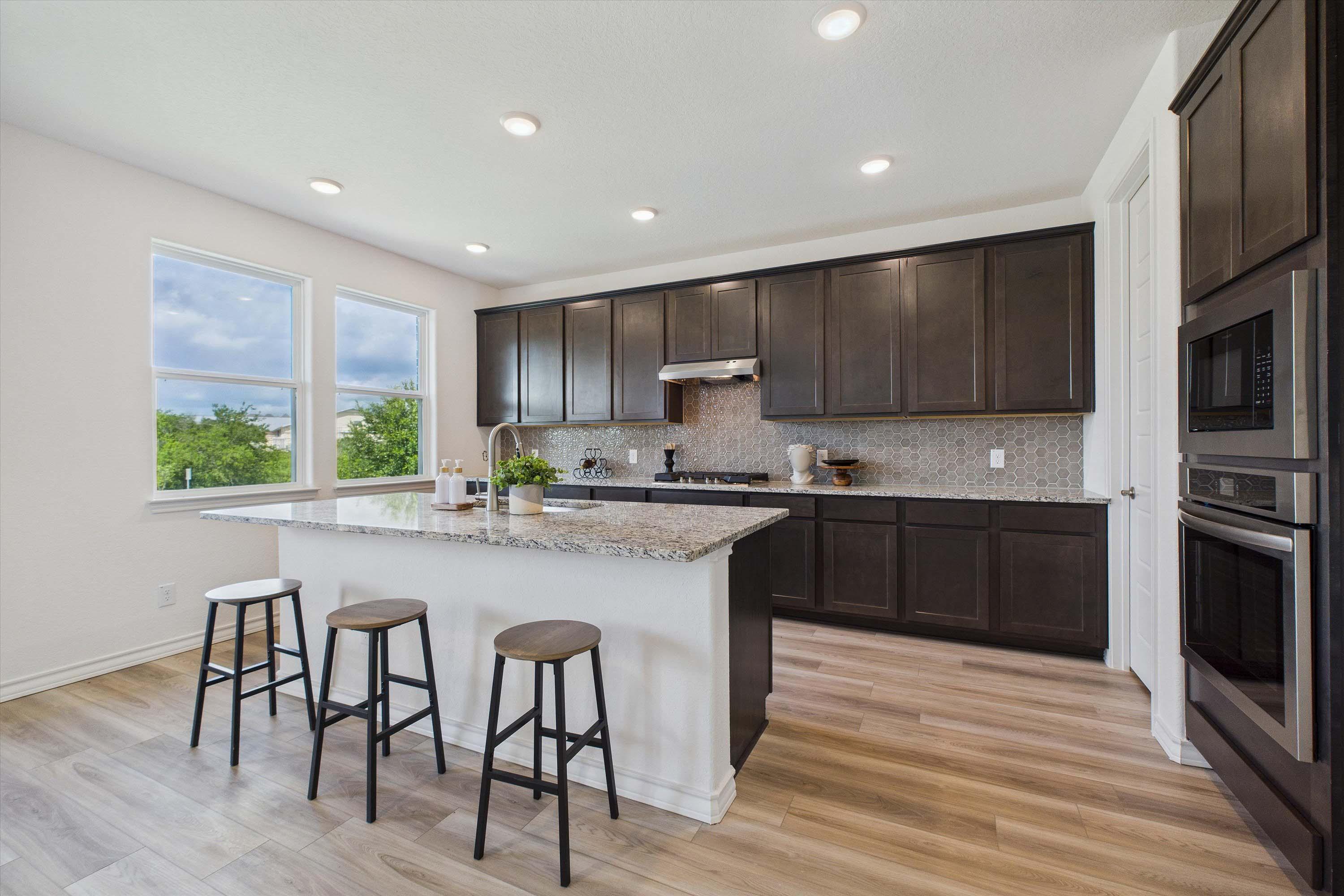 Modern kitchen in The Danbury featuring dark wood cabinets, granite island, and bar seating in Castroville, Texas.