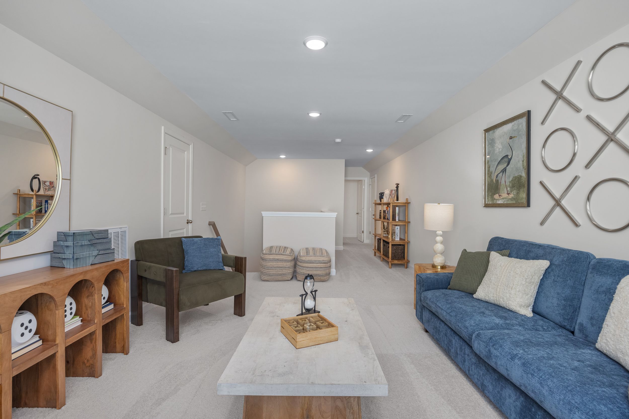 Cozy bonus room at Sage on North Main in Wake Forest NC with blue velvet sofa, wooden shelves, round mirror, and modern decor
