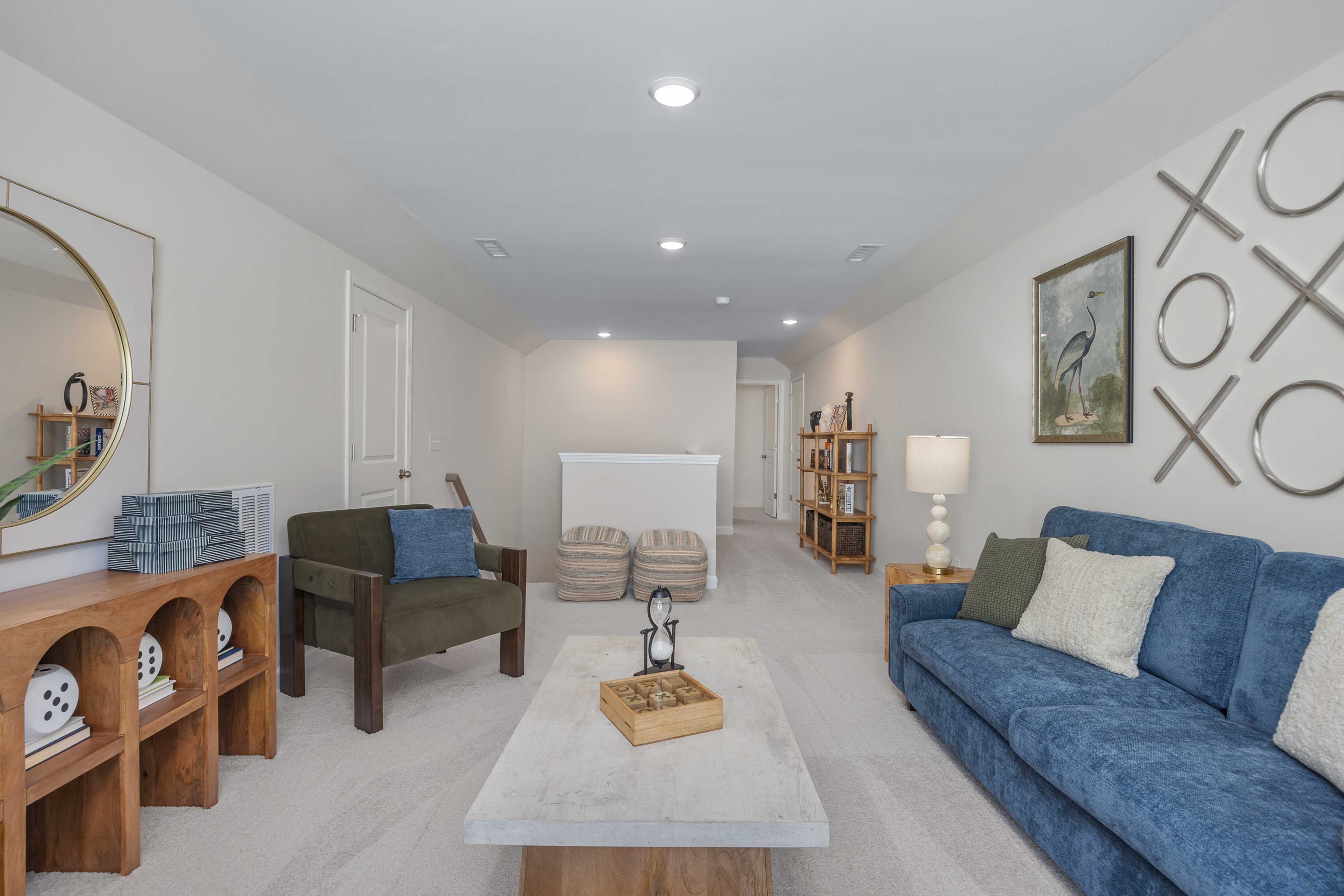 Cozy bonus room at Sage on North Main in Wake Forest NC with blue velvet sofa, wooden shelves, round mirror, and modern decor