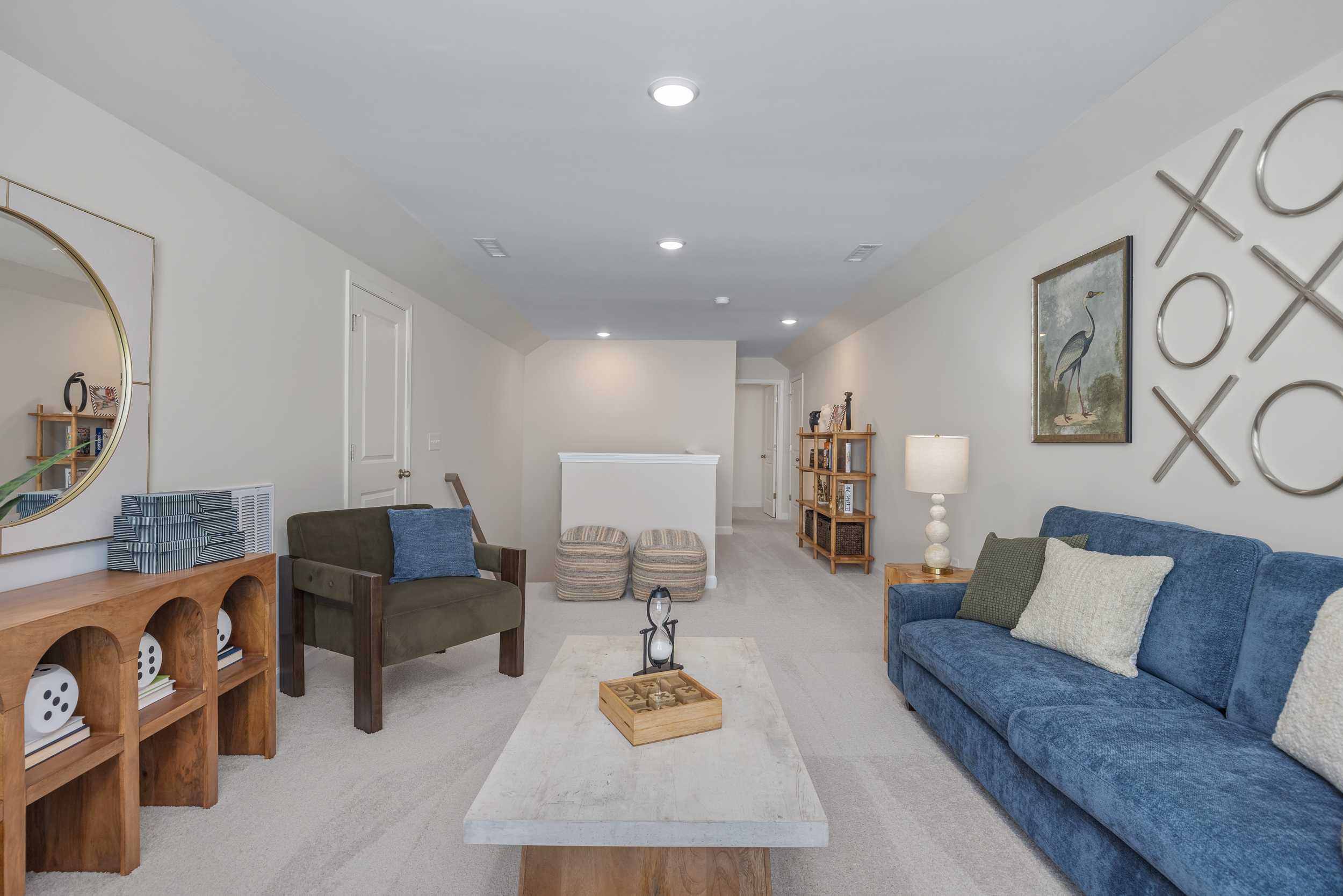 Cozy bonus room at Sage on North Main in Wake Forest NC with blue velvet sofa, wooden shelves, round mirror, and modern decor