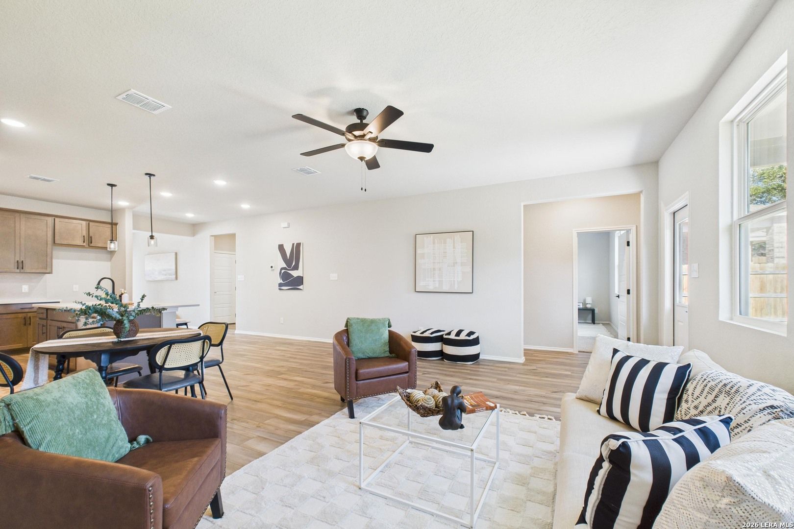 Open-concept living room with leather armchair, striped sofa, ceiling fan, and kitchen in Davidson Homes The Douglas E, Bricewood, San Antonio