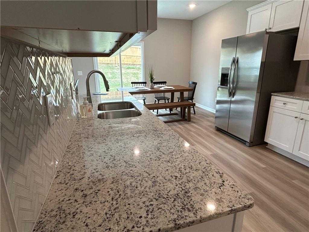 Open-concept kitchen with granite countertops, herringbone backsplash, stainless appliances, and adjacent dining area in The Bartlett, Phenix City, AL