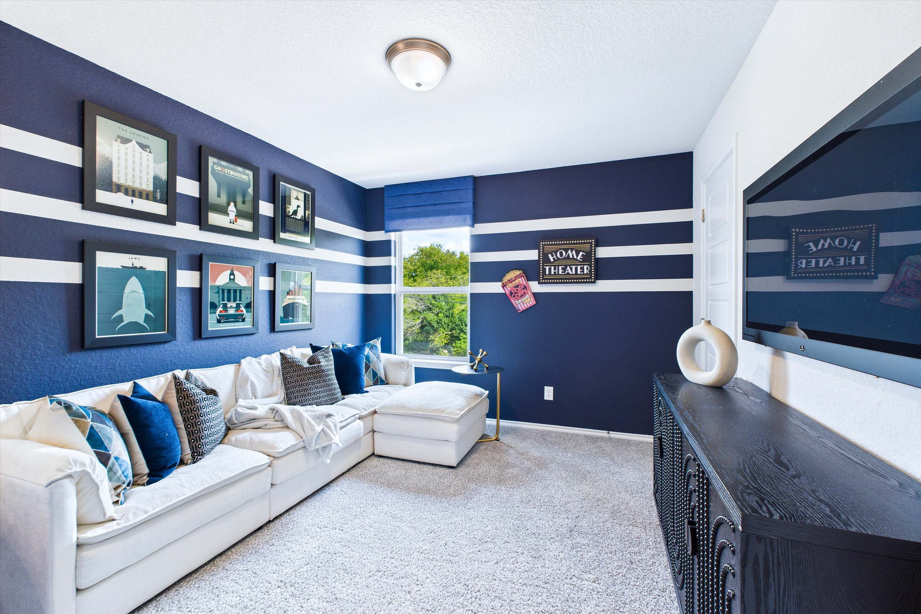 Cozy home theater room in The Gillian C by Davidson Homes, featuring striped blue walls, sectional seating, and TV.
