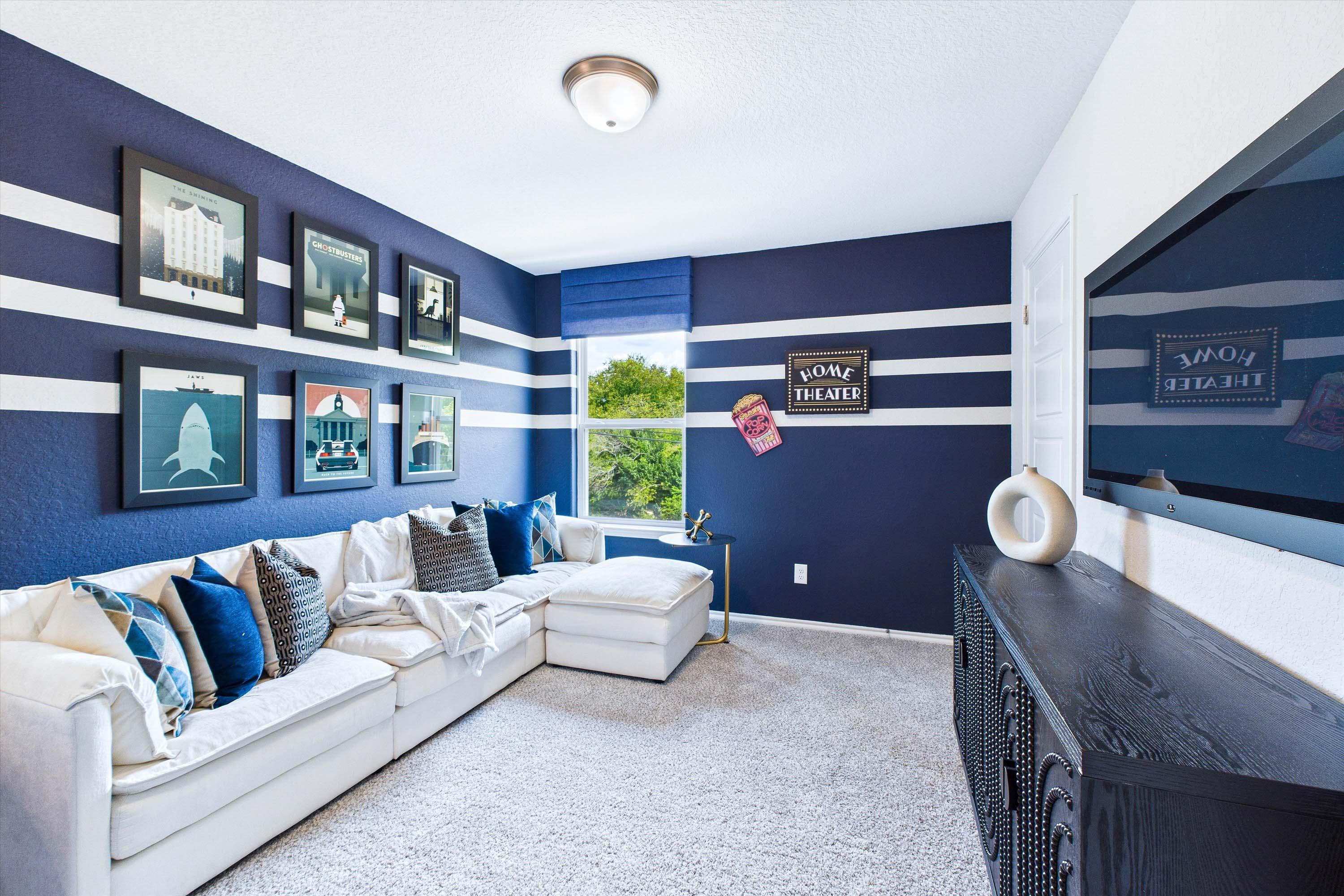 Cozy home theater room in The Gillian C by Davidson Homes, featuring striped blue walls, sectional seating, and TV.