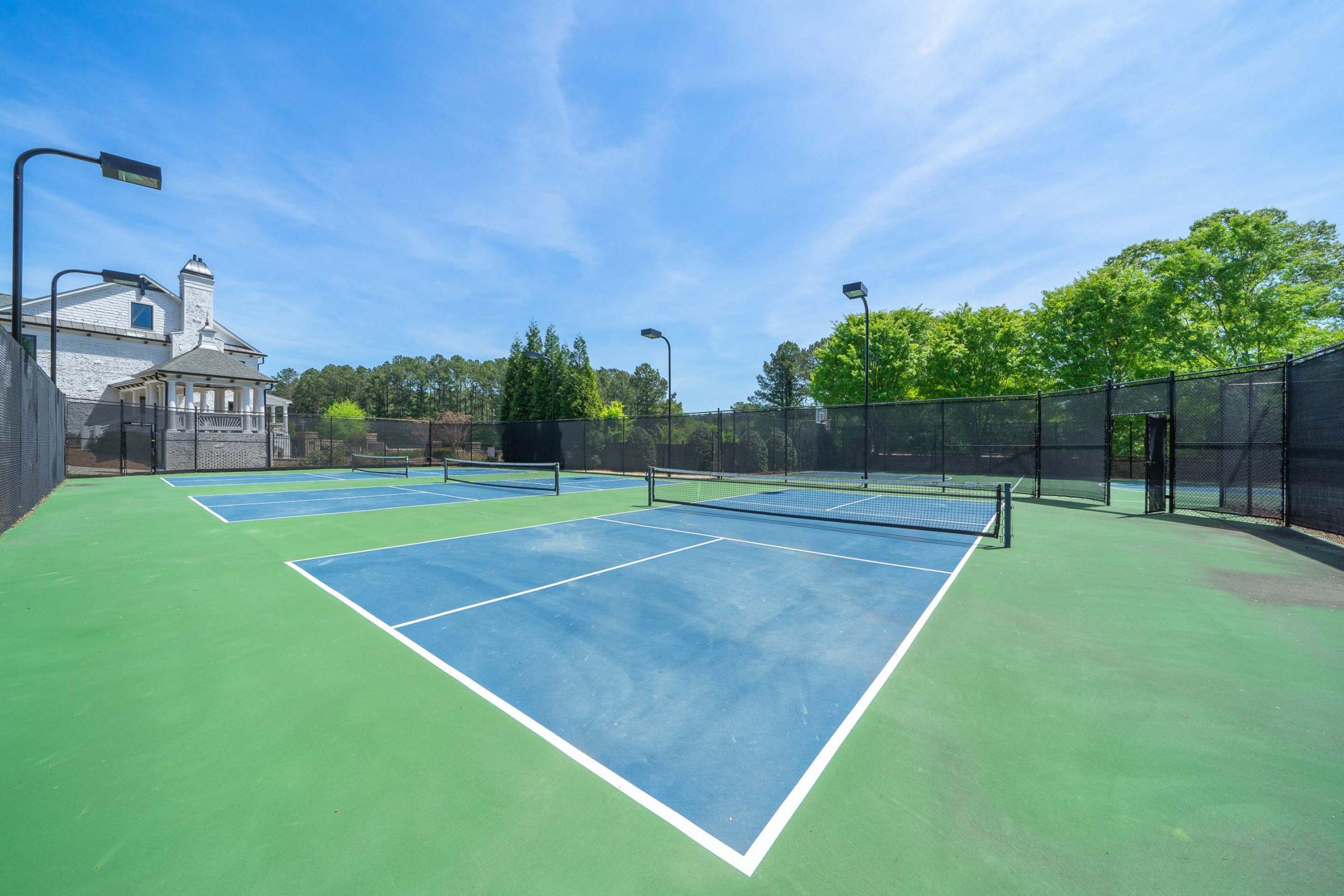 Tennis courts at Mountainbrook in Cartersville GA with blue surfaces, black fencing, lighting poles, and surrounding trees