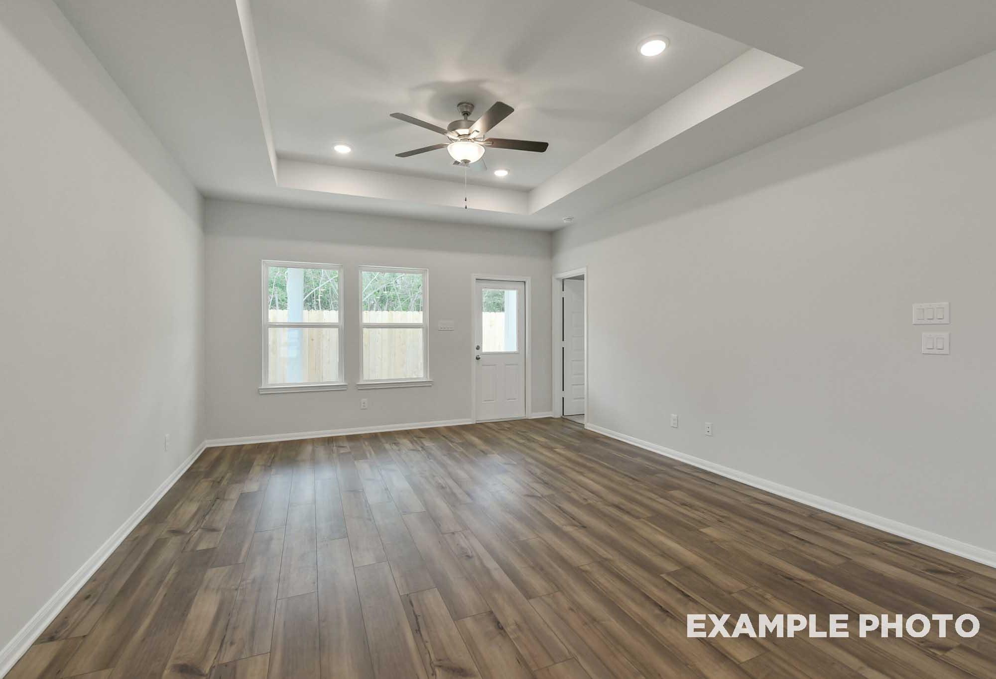 Spacious living area in The Frio floor plan featuring a tray ceiling, wood-look flooring, and natural light.