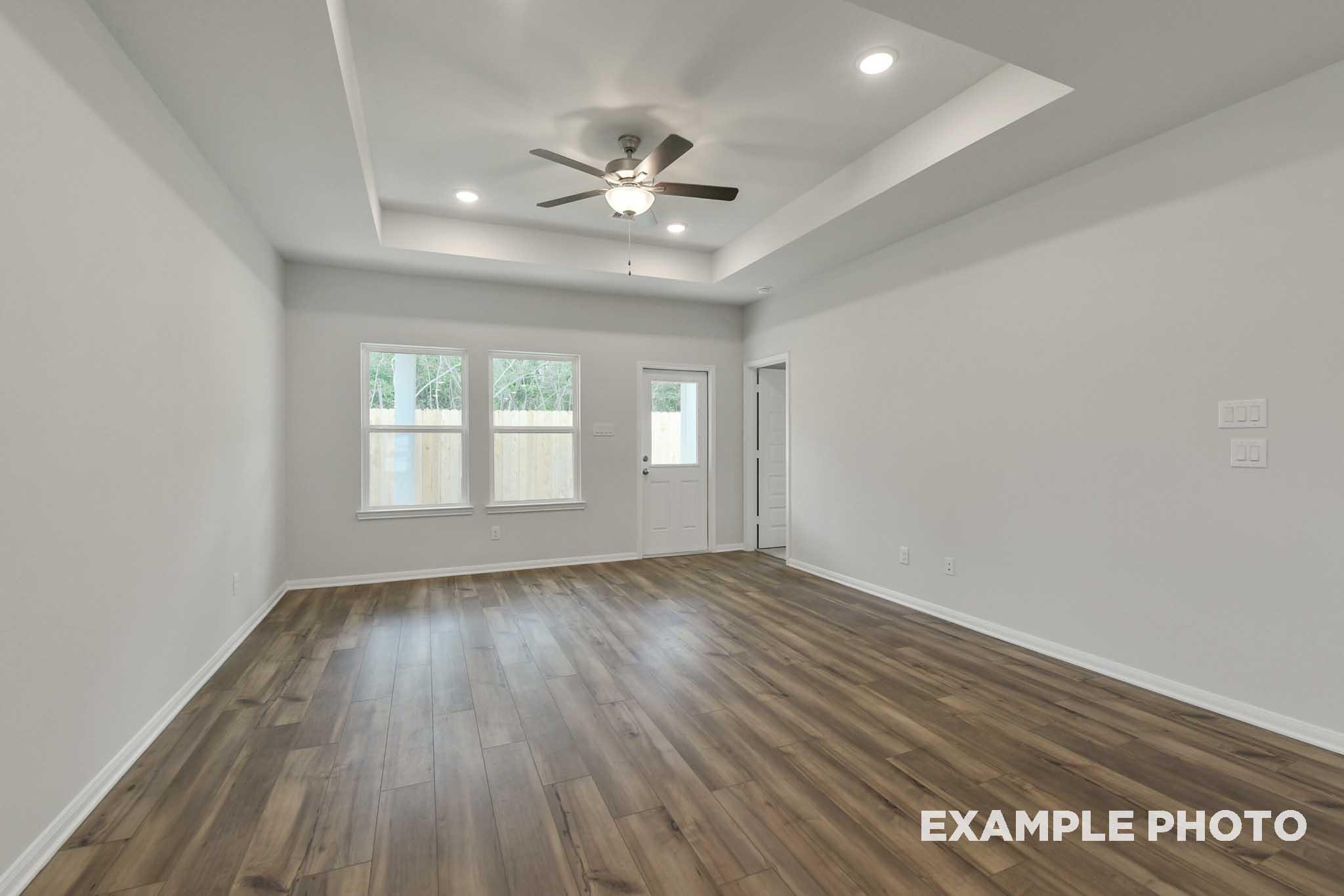 Spacious living area in The Frio floor plan featuring a tray ceiling, wood-look flooring, and natural light.
