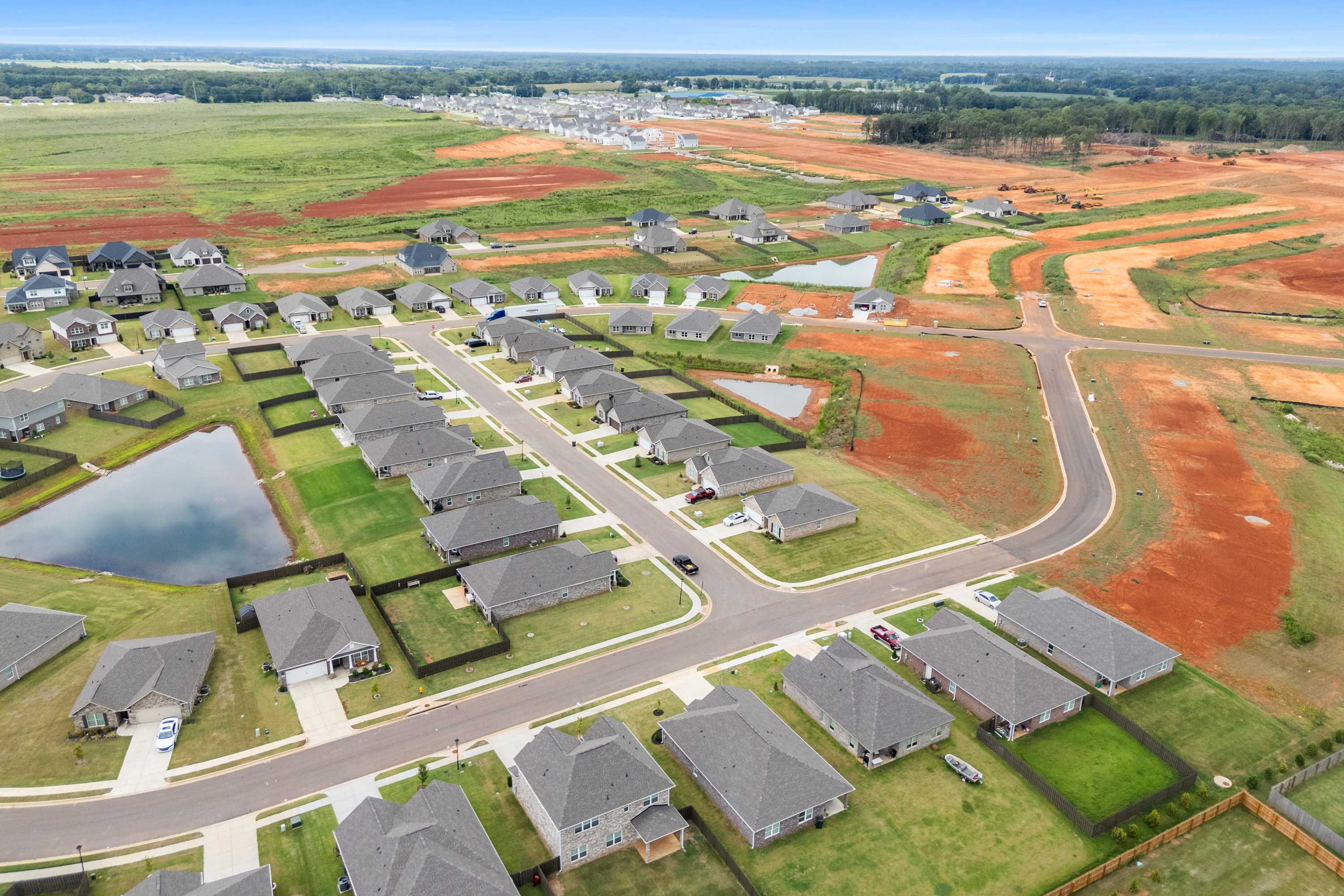 Aerial view of Heritage Lakes in New Market Alabama with new Davidson Homes, pond, streets and red clay fields