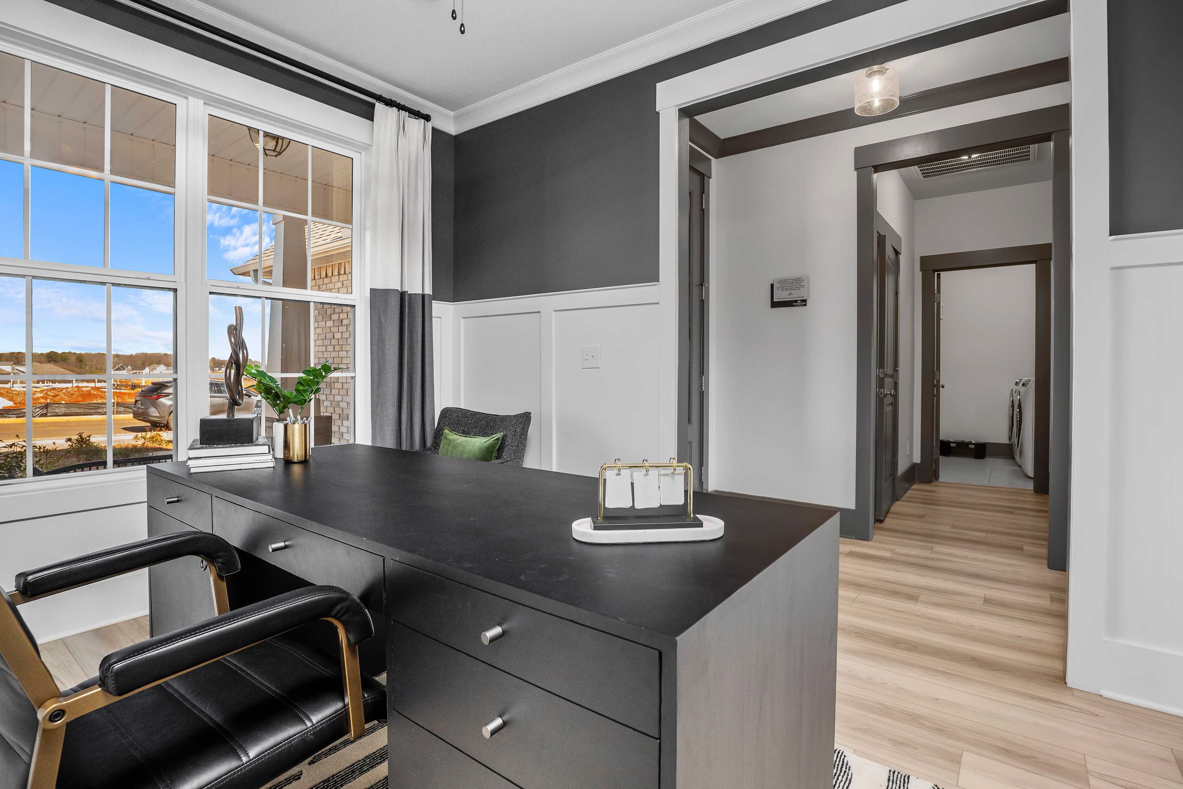 Spacious home office at Barnett's Crossing in Madison, Alabama with black desk, leather chair, large windows, and hardwood floors