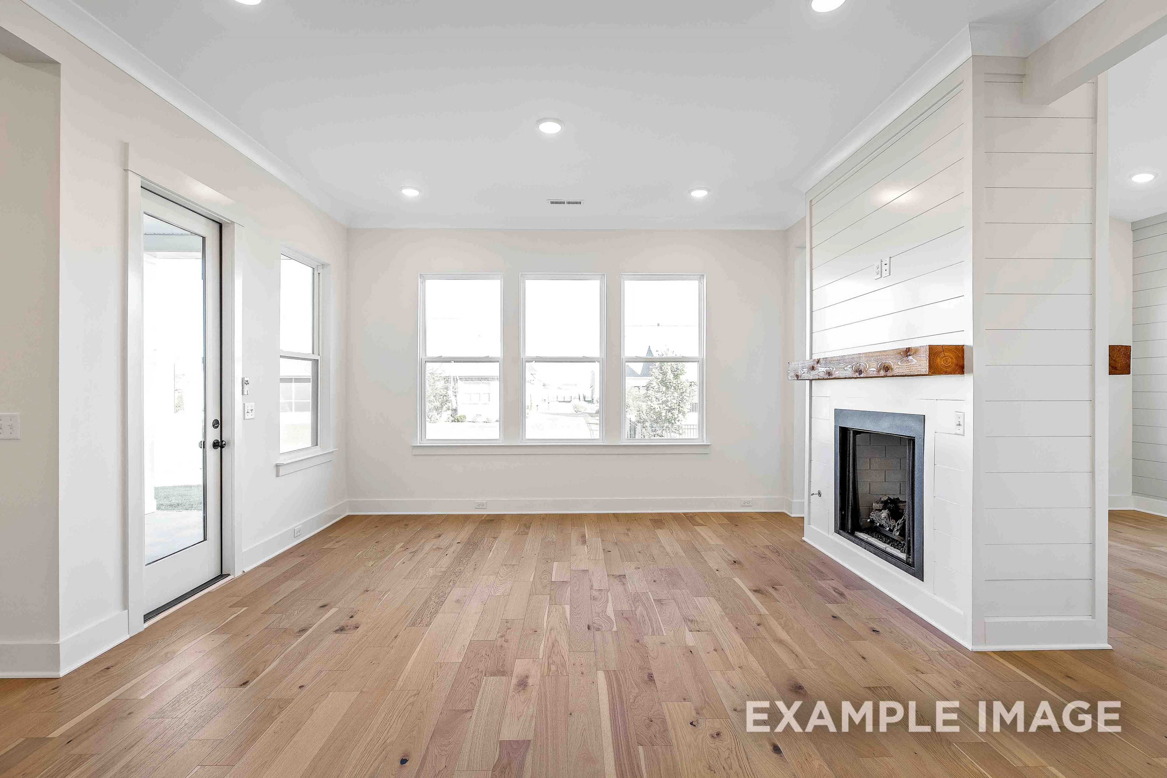 Spacious living room in The Albany A with hardwood floors, shiplap fireplace wall, large windows, and French doors