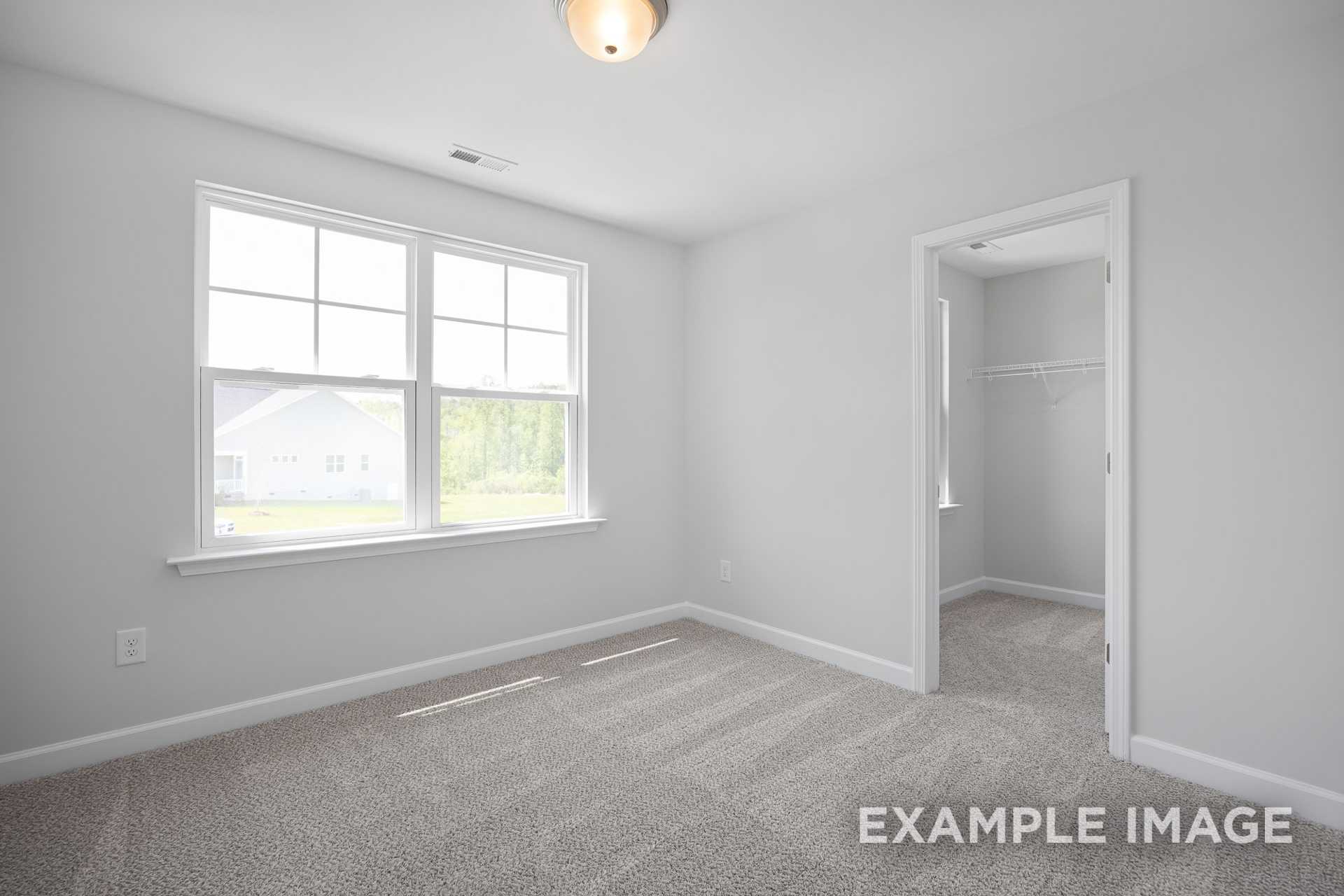 Spacious bedroom in The Grace C with light gray walls, large windows, neutral carpet, and adjacent walk-in closet by Davidson Homes