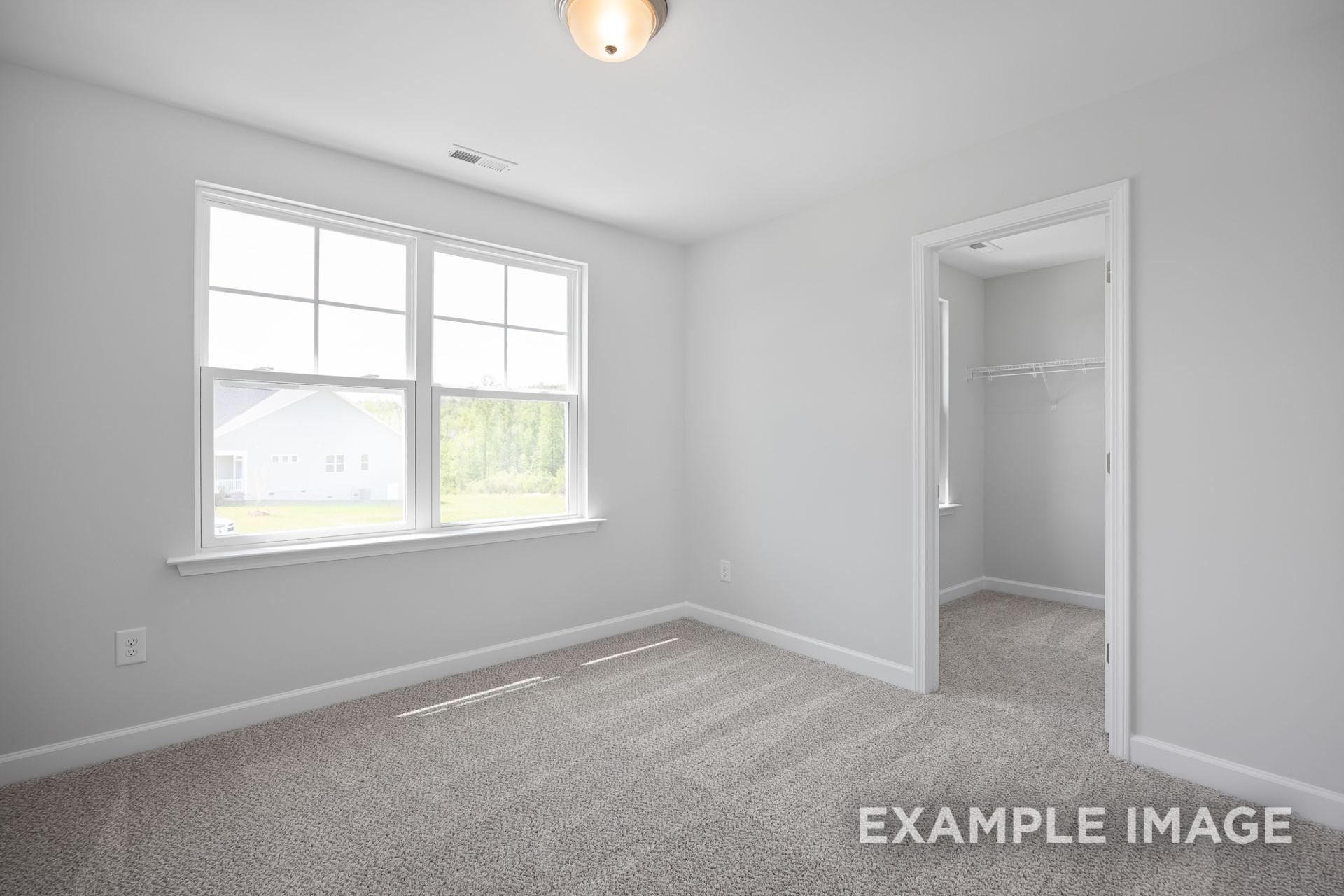 Spacious bedroom in The Grace C with light gray walls, large windows, neutral carpet, and adjacent walk-in closet by Davidson Homes