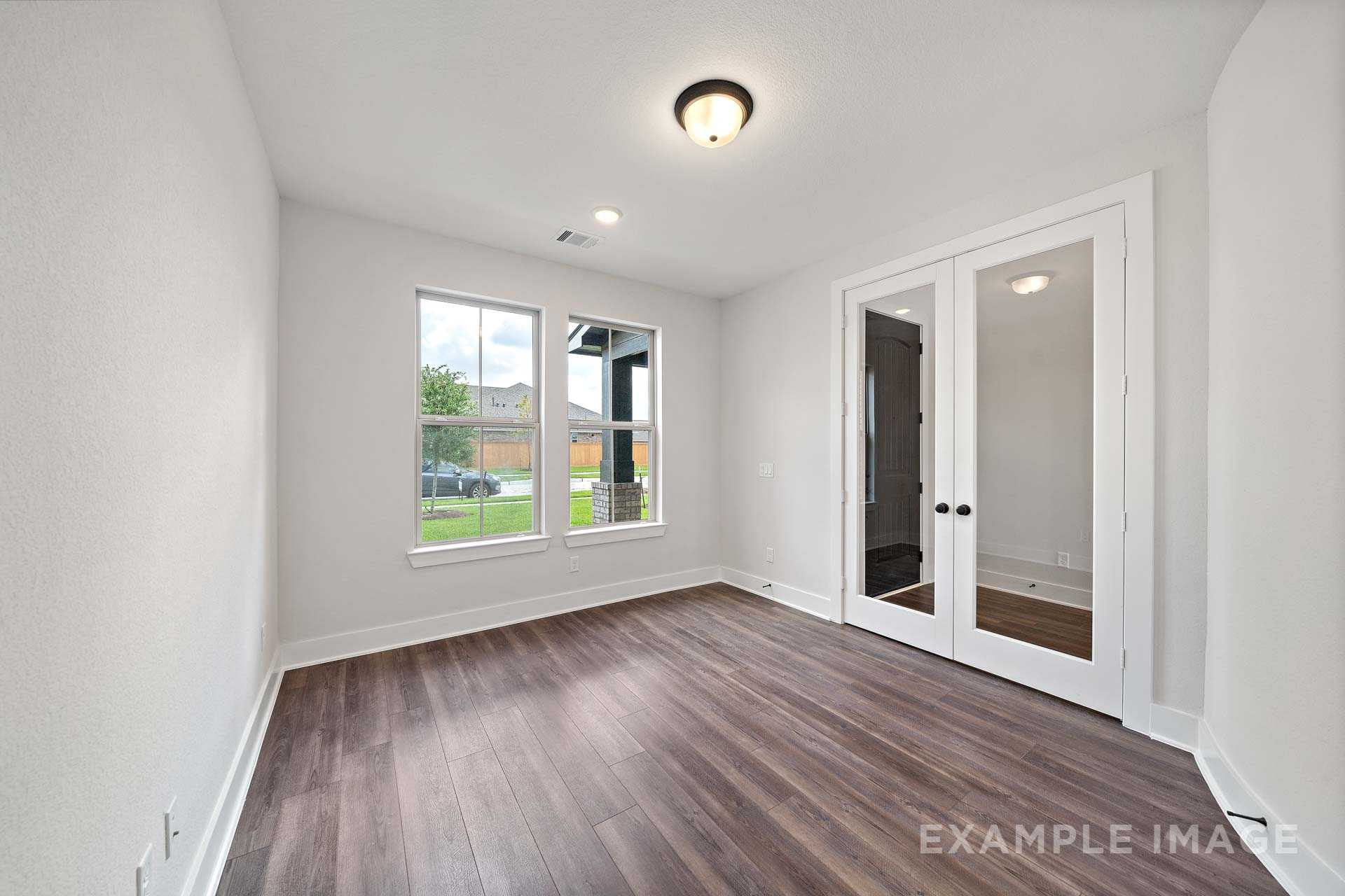 Spacious master bedroom in The Victoria by Davidson Homes, featuring hardwood floors, large windows with green views, and glass double doors