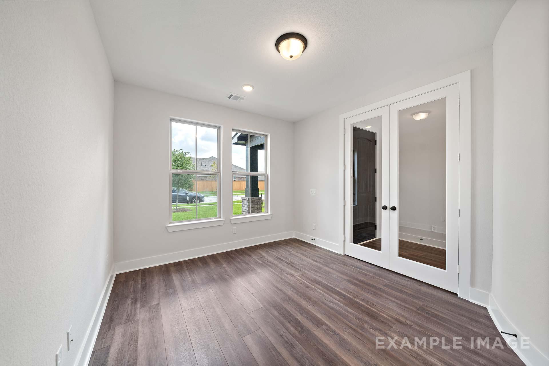 Spacious master bedroom in The Victoria by Davidson Homes, featuring hardwood floors, large windows with green views, and glass double doors