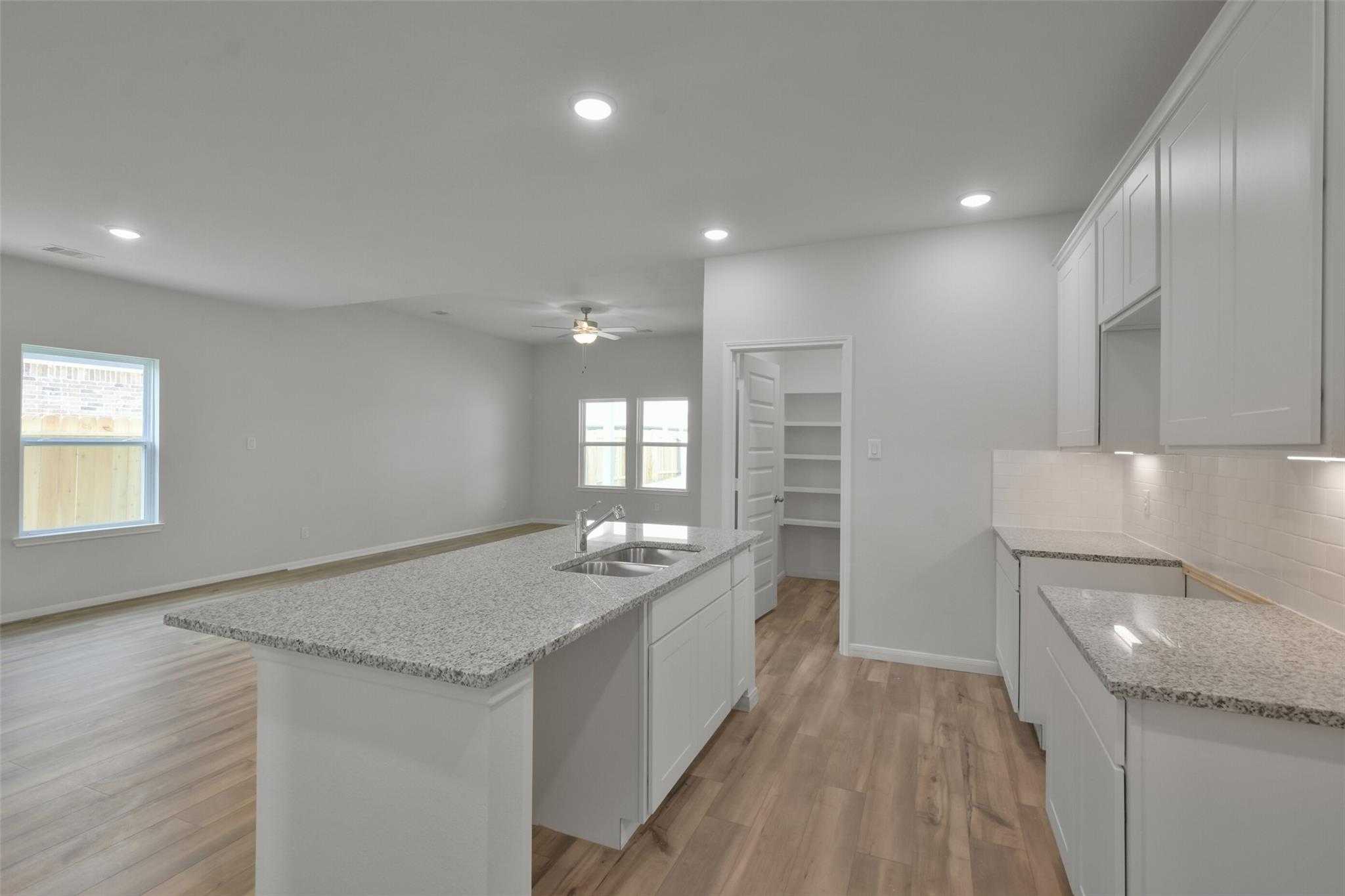 Spacious open-concept kitchen with granite countertops, white cabinets, and island in Davidson Homes The Tierra A, Dayton, Texas