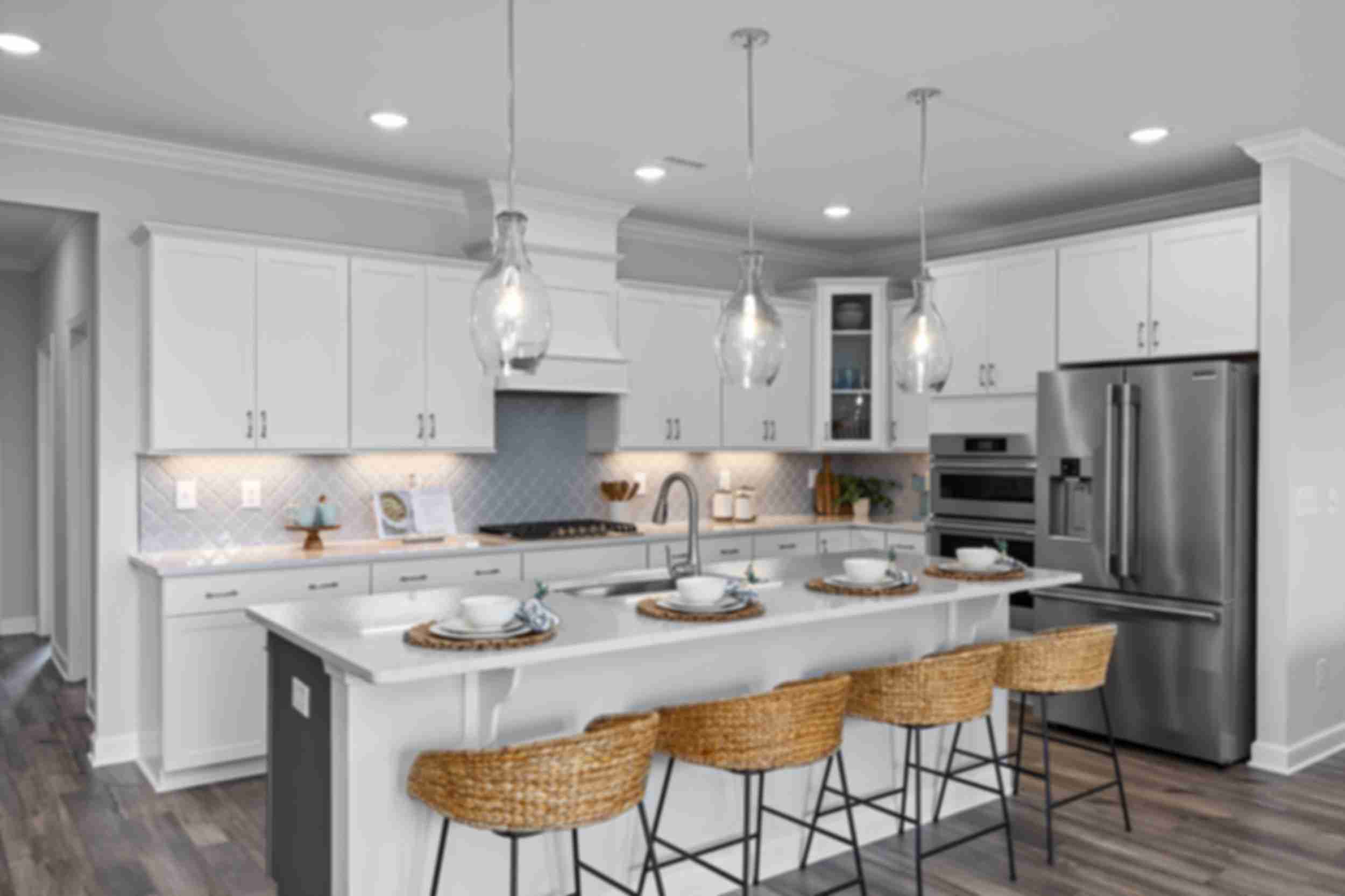 Modern white kitchen in Tobacco Road Angier NC by Davidson Homes with island bar stools pendant lights and stainless appliances