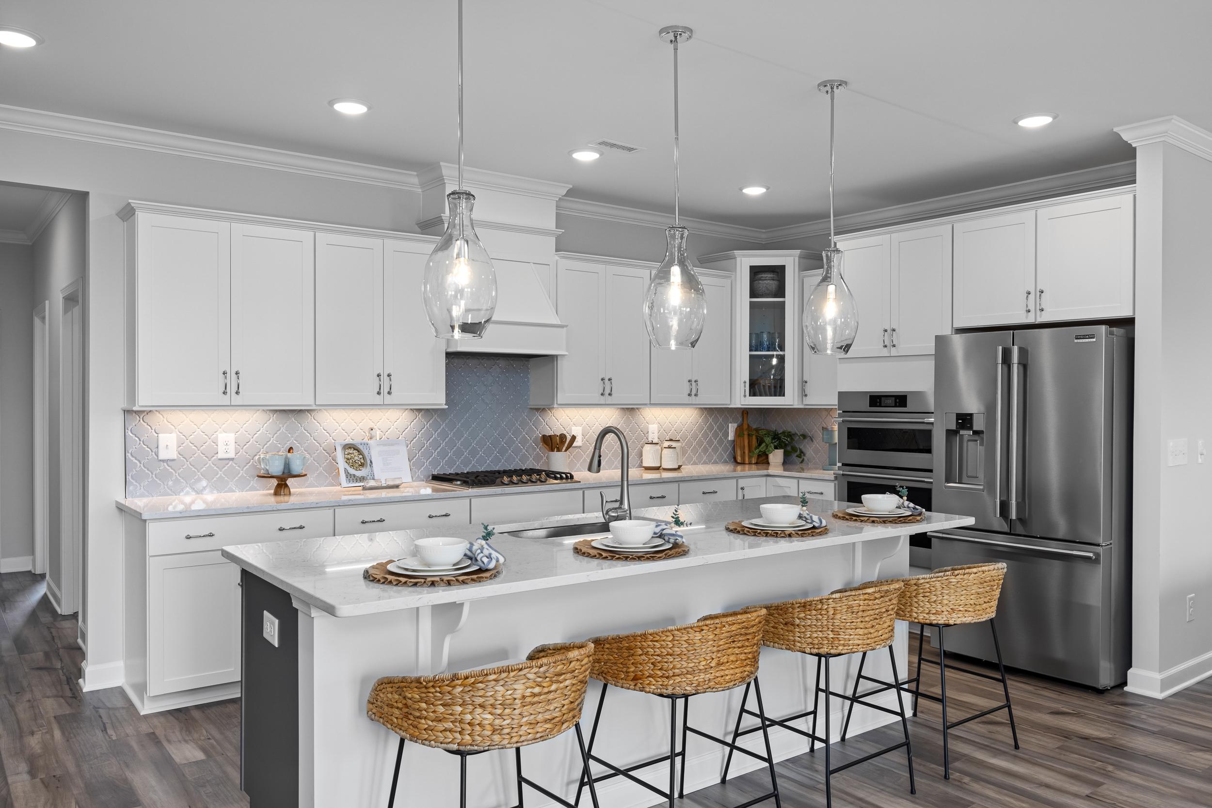 Modern white kitchen in Tobacco Road Angier NC by Davidson Homes with island bar stools pendant lights and stainless appliances