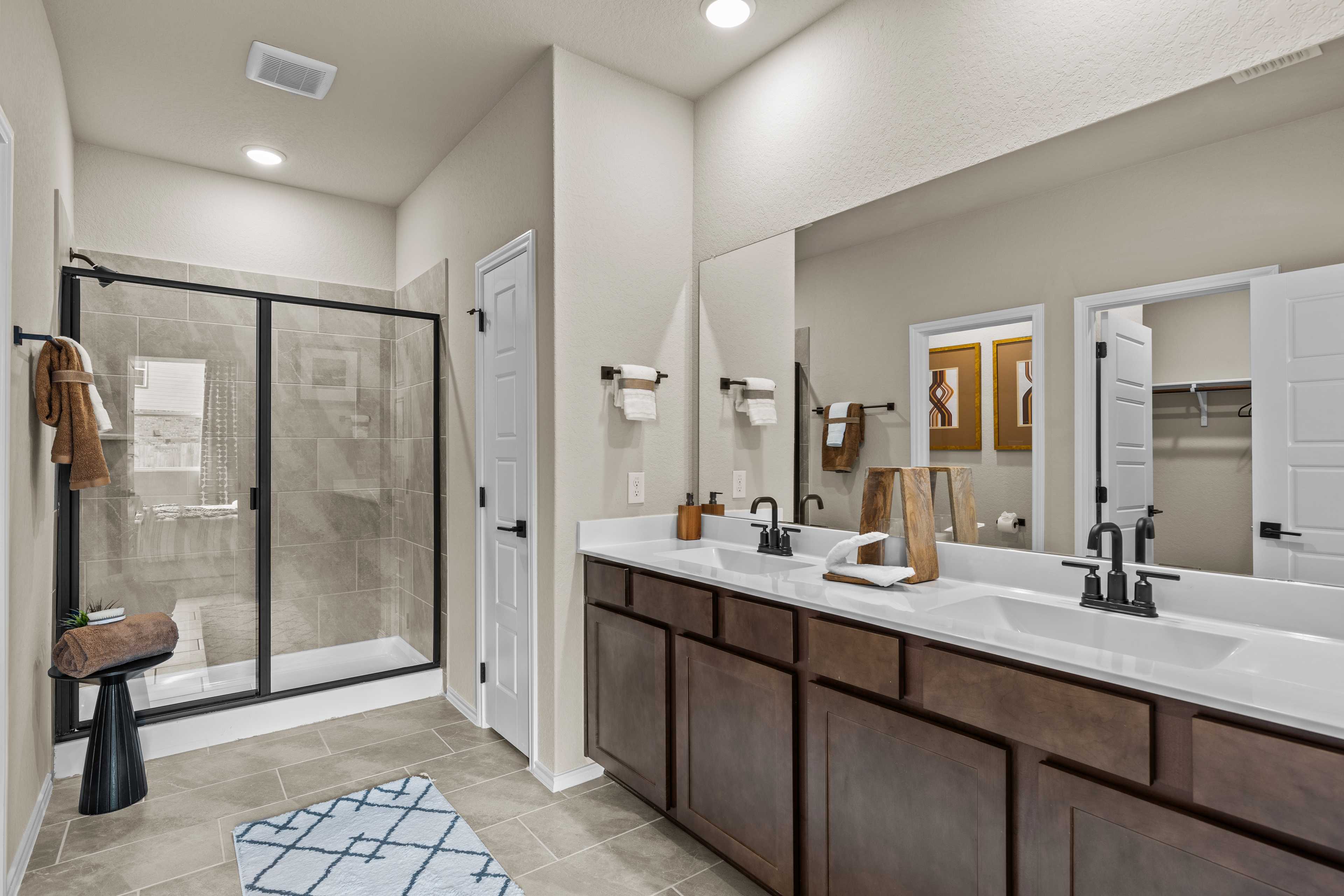 Modern master bathroom at Bricewood in San Antonio TX with double vanity, glass walk-in shower, and wood cabinets by Davidson Homes